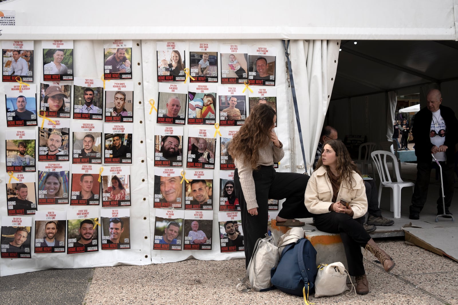 Women sit near posters of hostages held by Hamas in the Gaza Strip, in Tel Aviv, Israel, as Israel's security cabinet convened to decide whether to approve a deal that would release dozens of hostages held by militants in Gaza and pause the 15-month-war, Friday, Jan. 17, 2025. (AP Photo/Maya Alleruzzo)