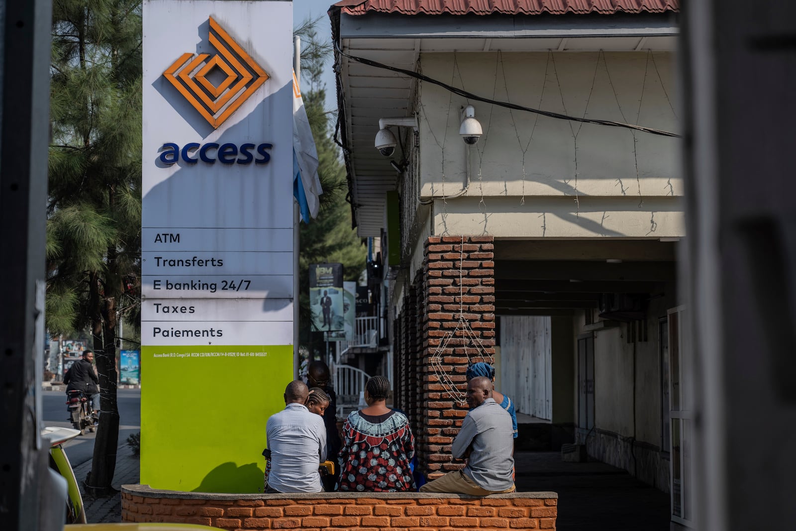 People sit in front of a non-functioning bank in downtown Goma, Democratic Republic of Congo, Thursday, Feb. 27, 2025, one month after Rwanda-backed M23 rebels captured the city. (AP Photo/Moses Sawasawa)