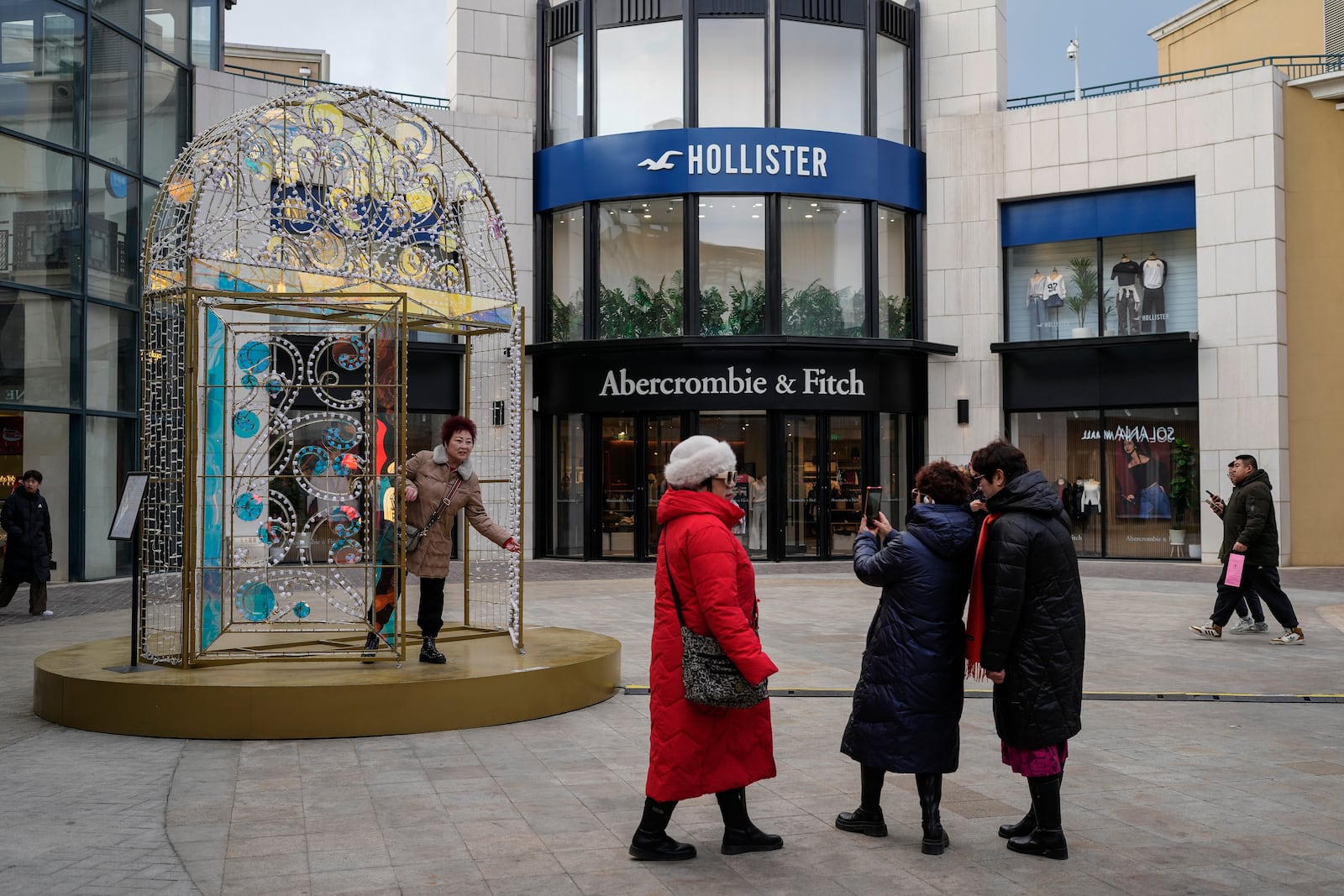 Women take a picture with a decoration on display near an American fashion boutiques at an outdoor shopping mall in Beijing, Tuesday, Feb. 4, 2025. (AP Photo/Andy Wong)