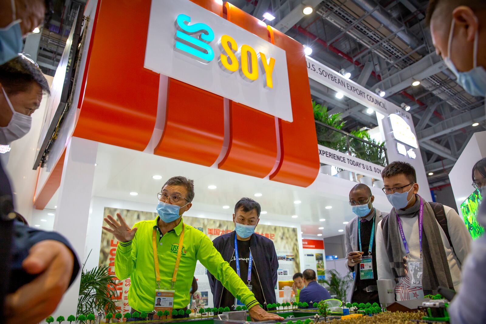 FILE - A staff member wearing a face mask talks to visitors at a display from the U.S. Soybean Export Council at the China International Import Expo in Shanghai, Nov. 5, 2020. (AP Photo/Mark Schiefelbein, File)