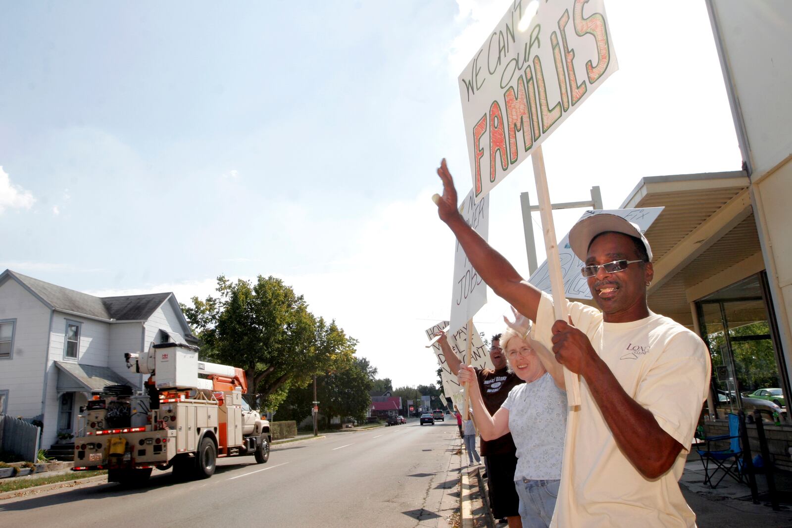 Carlos Cain, and about 20 other employees of Long Cleaners in Miamisburg, wave to utility trucks from New Hampshire as they drive down Main St. in front of the store Sunday Sept. 21. Employees of the store protested in the afternoon because they have had no power for a week since a windstorm hit Sunday Sept. 14 and have been unable to work. Staff photo by Lisa Powell