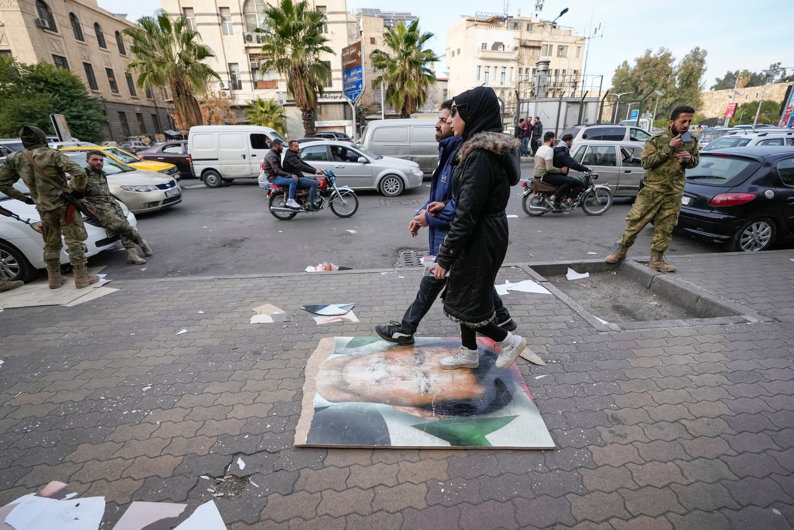 Pedestrians casually walk over an image of former Syrian President Bashar Assad on a sidewalk in Damascus, Syria, Tuesday, Dec. 10, 2024. (AP Photo/Hussein Malla)