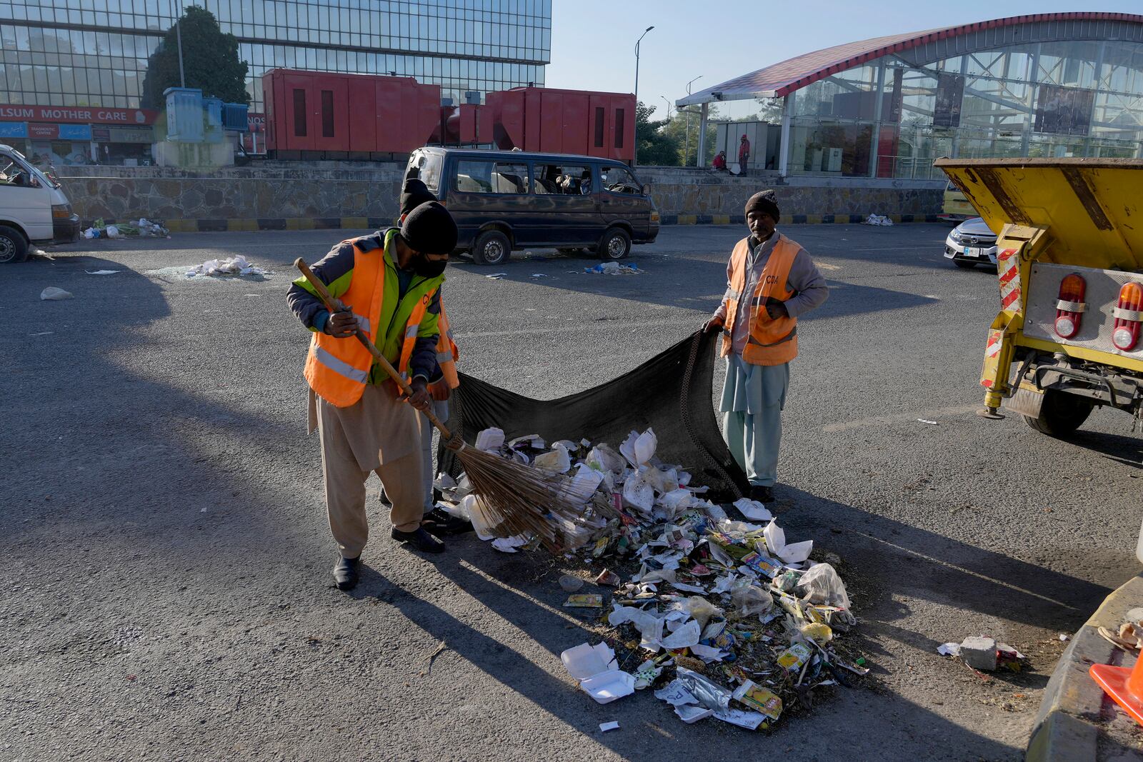 Workers clean an area near the damaged vehicles left behind by supporters of imprisoned former Prime Minister Imran Khan's Pakistan Tehreek-e-Insaf party when security forces launched an operation Tuesday night to disperse them, in Islamabad, Pakistan, Wednesday, Nov. 27, 2024. (AP Photo/Anjum Naveed)