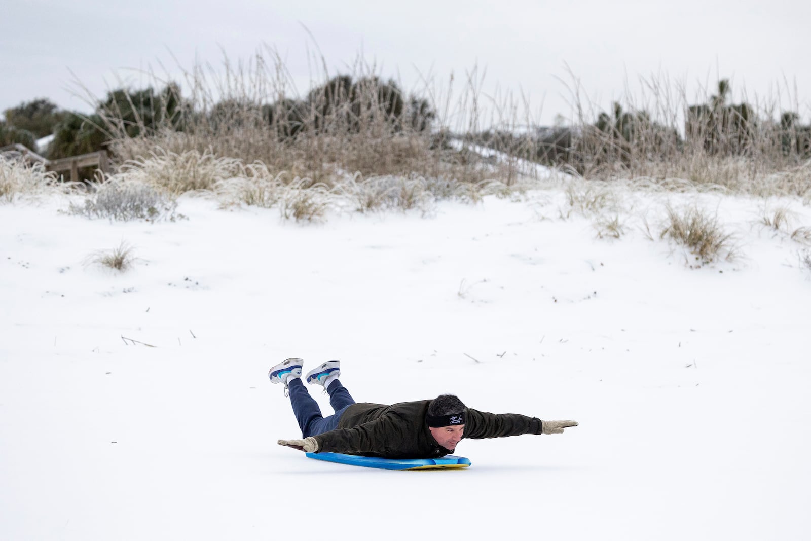 Alex Spiotta, from the Isle of Palms, S.C., uses a boogie board to sled across the beach after a winter storm dropped ice and snow Wednesday, Jan. 22, 2025, on the Isle of Palms, S.C. (AP Photo/Mic Smith)