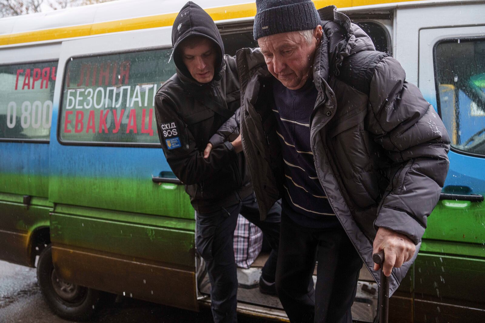 A volunteer of east SOS NGO helps en elderly man to walks out from a bus after evacuation from the frontline at a center for displaced people in Pavlohrad, Ukraine, Saturday, Feb. 1, 2024. (AP Photo/Evgeniy Maloletka)