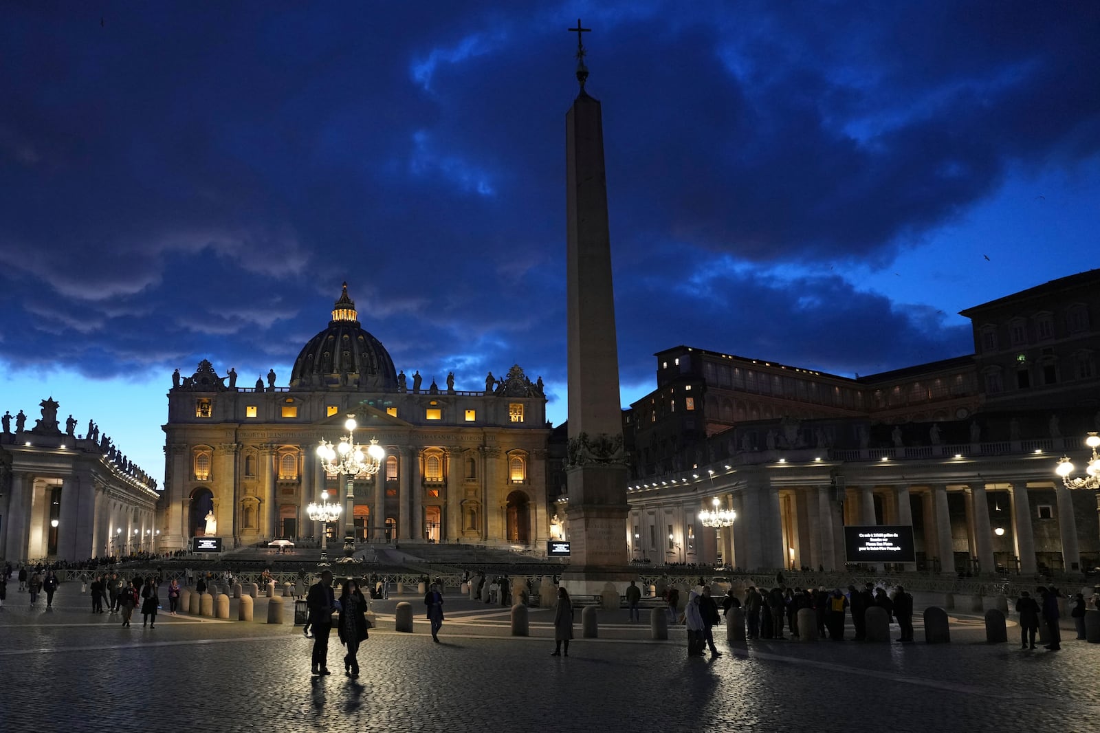 People walk at dusk in St Peter's Square at The Vatican, Thursday, Feb. 27, 2025. (AP Photo/Kirsty Wigglesworth)