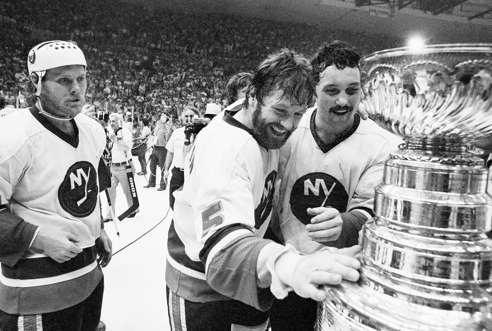 FILE - New York Islanders captain Denis Potvin (5) reaches out to touch the Stanley Cup trophy as teammate Brian Trottier looks on after the Islanders won the NHL championship at Nassau Coliseum in Uniondale, N.Y. Saturday, May 24, 1980. (AP Photo/Richard Drew, File)