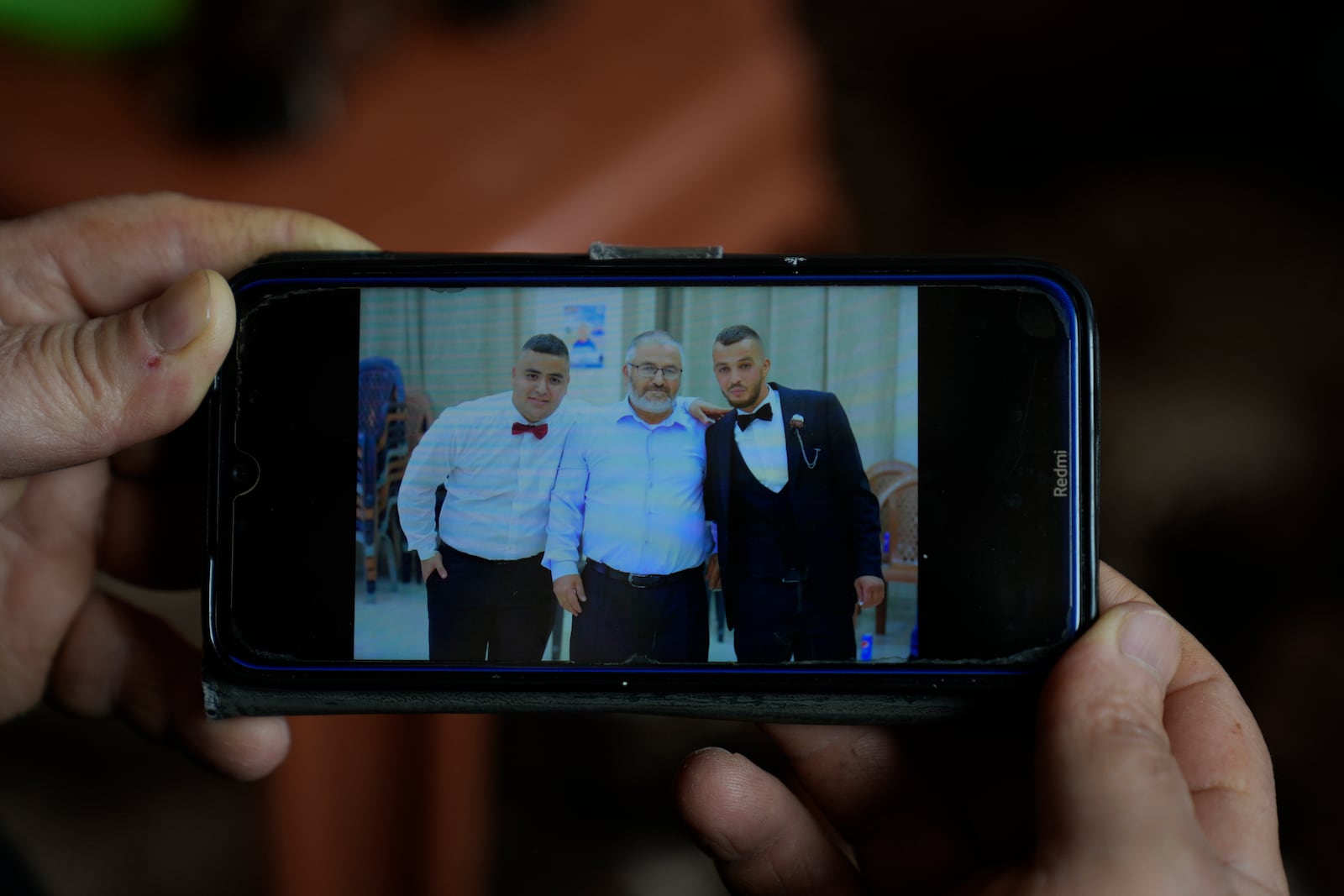 Mohammed Shula displays a picture on his cellphone of him, center and his sons Bilal and Yazan, inside a relative's house where he and his wife have taken refuge in the West Bank village of Kafr al-Labad, Monday, Feb. 10, 2025. (AP Photo/Nasser Nasser)