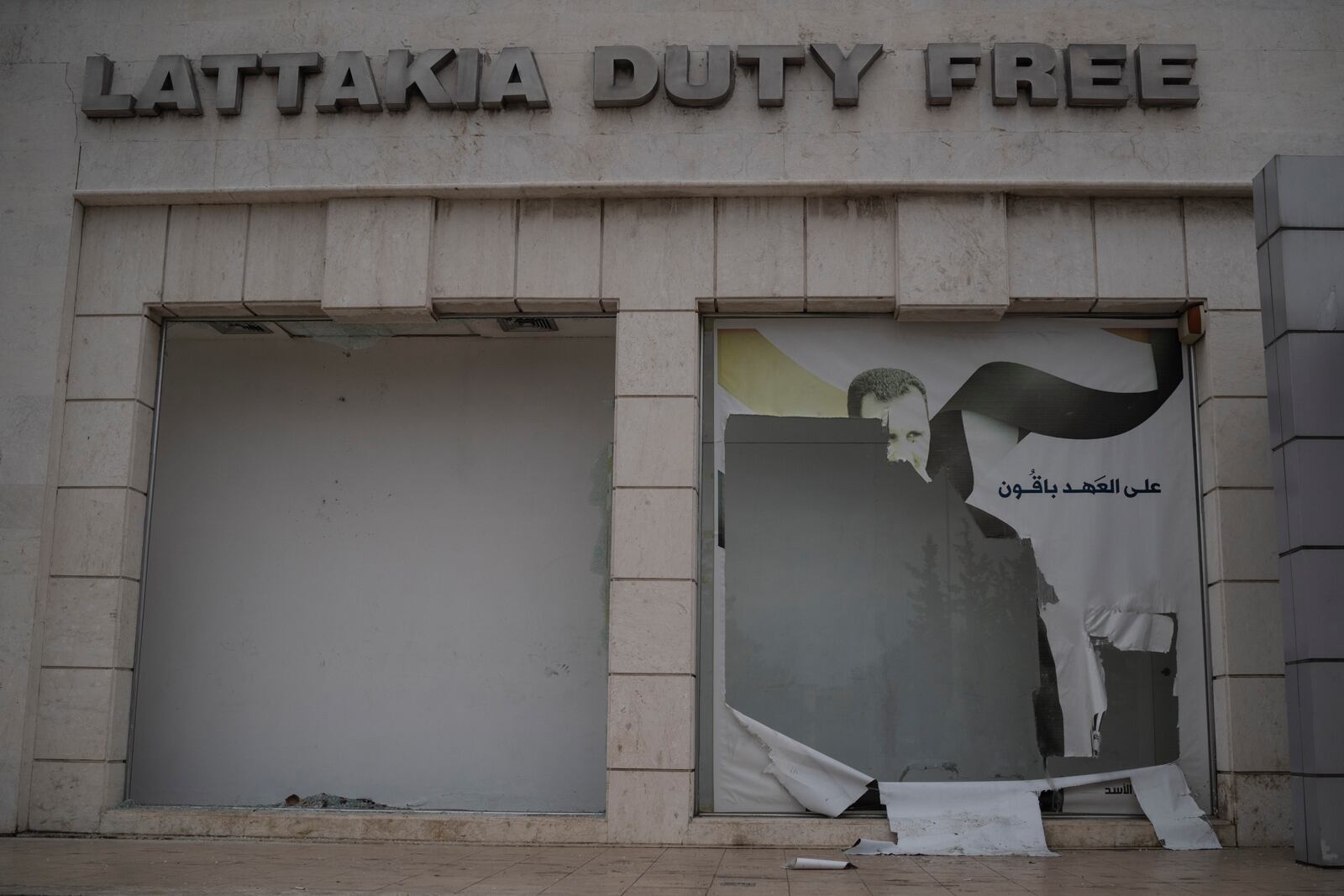 A damaged shop window with an image depicting Bashar Assad is seen at the port of Latakia, Syria, Monday, Dec. 16, 2024. (AP Photo/Leo Correa)