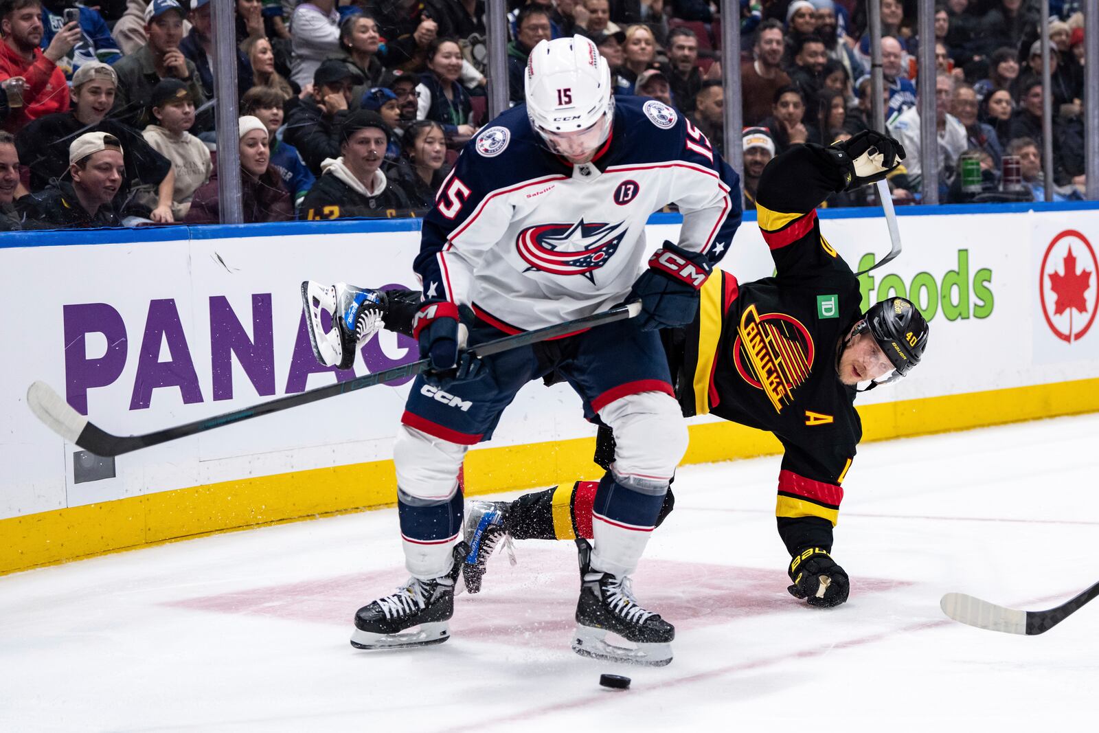 Vancouver Canucks' Elias Pettersson (40) falls as Columbus Blue Jackets' Dante Fabbro (15) skates with the puck during the third period of an NHL hockey game in Vancouver, British Columbia, Friday, Dec. 6, 2024. (Ethan Cairns/The Canadian Press via AP)