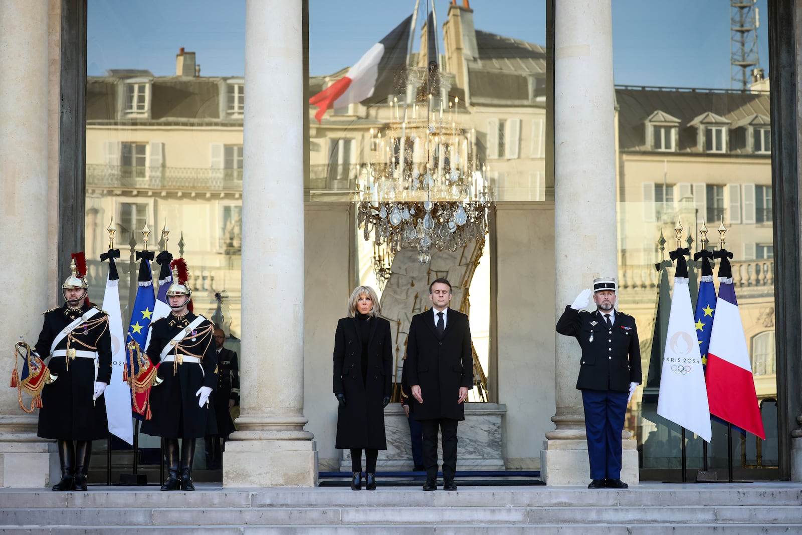 French President Emmanuel Macron and his wife Brigitte Macron stand for a minute of silence Monday, Dec. 23, 2024 at the Elysee Palace, where the French flag flies halfmast, in Paris, after Macron declared a day of national mourning for the lives lost when Cyclone Chido ripped through the Indian Ocean territory of Mayotte. (AP Photo/Thomas Padilla, Pool)