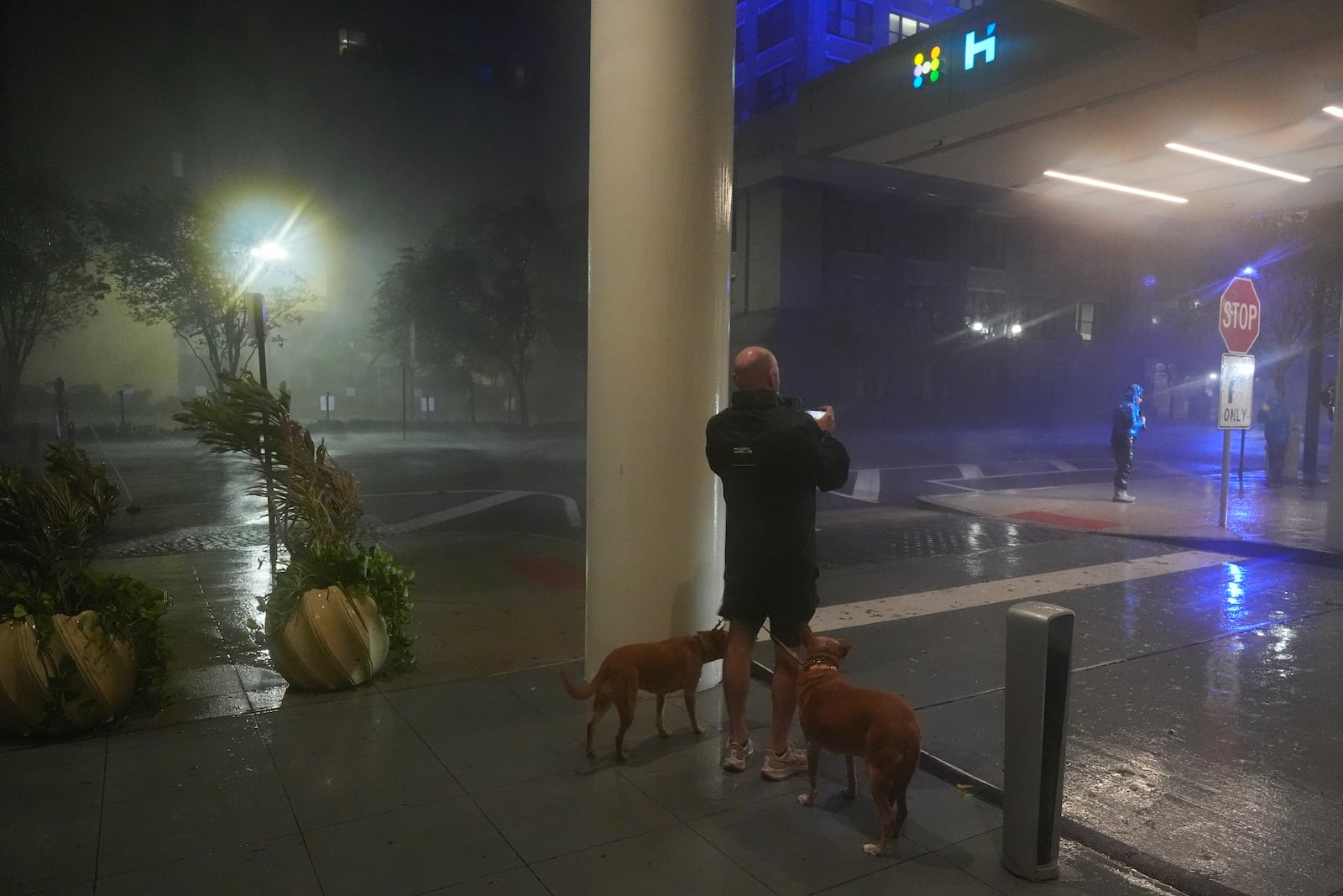 A man walking his dogs takes a picture from the sheltered entryway of the Hyatt Place Downtown Tampa hotel, as strong gusts of wind from Hurricane Milton blow sheets of rain along the street in Tampa, Fla., Wednesday, Oct. 9, 2024. (AP Photo Rebecca Blackwell)