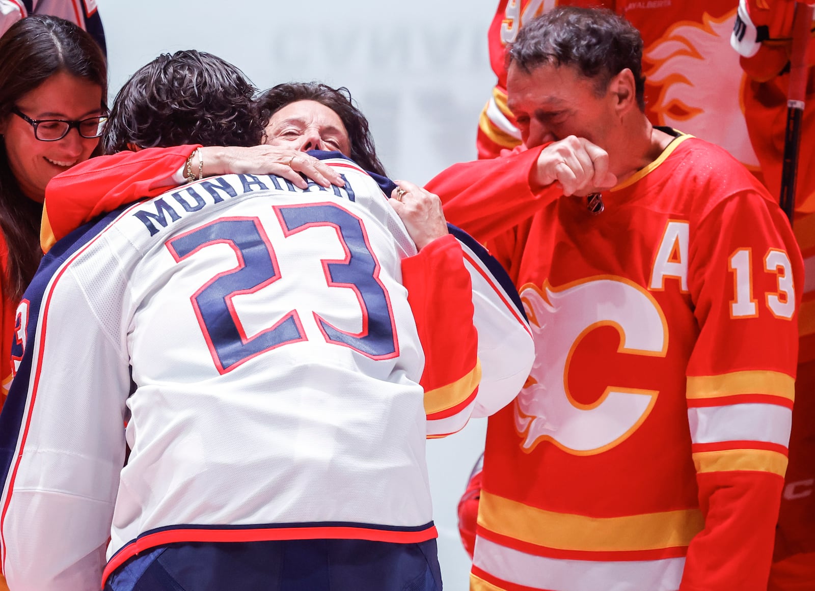 Columbus Blue Jackets' Sean Monahan (23) hugs Johnny Gaudreau's mother Jane as his father Guy, right, looks on at centre ice prior to first period NHL hockey action against the Calgary Flames in Calgary on Tuesday, Dec. 3, 2024.THE CANADIAN PRESS/Jeff McIntosh/The Canadian Press via AP)