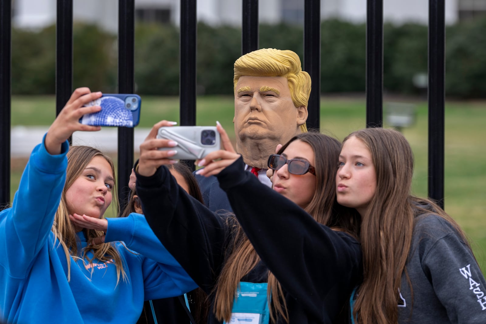 A group of young visitors poses for a photo with another visitor to the city wearing a mask of President Donald Trump in front of the White House in Washington, Thursday, March 13, 2025. (AP Photo/Ben Curtis)