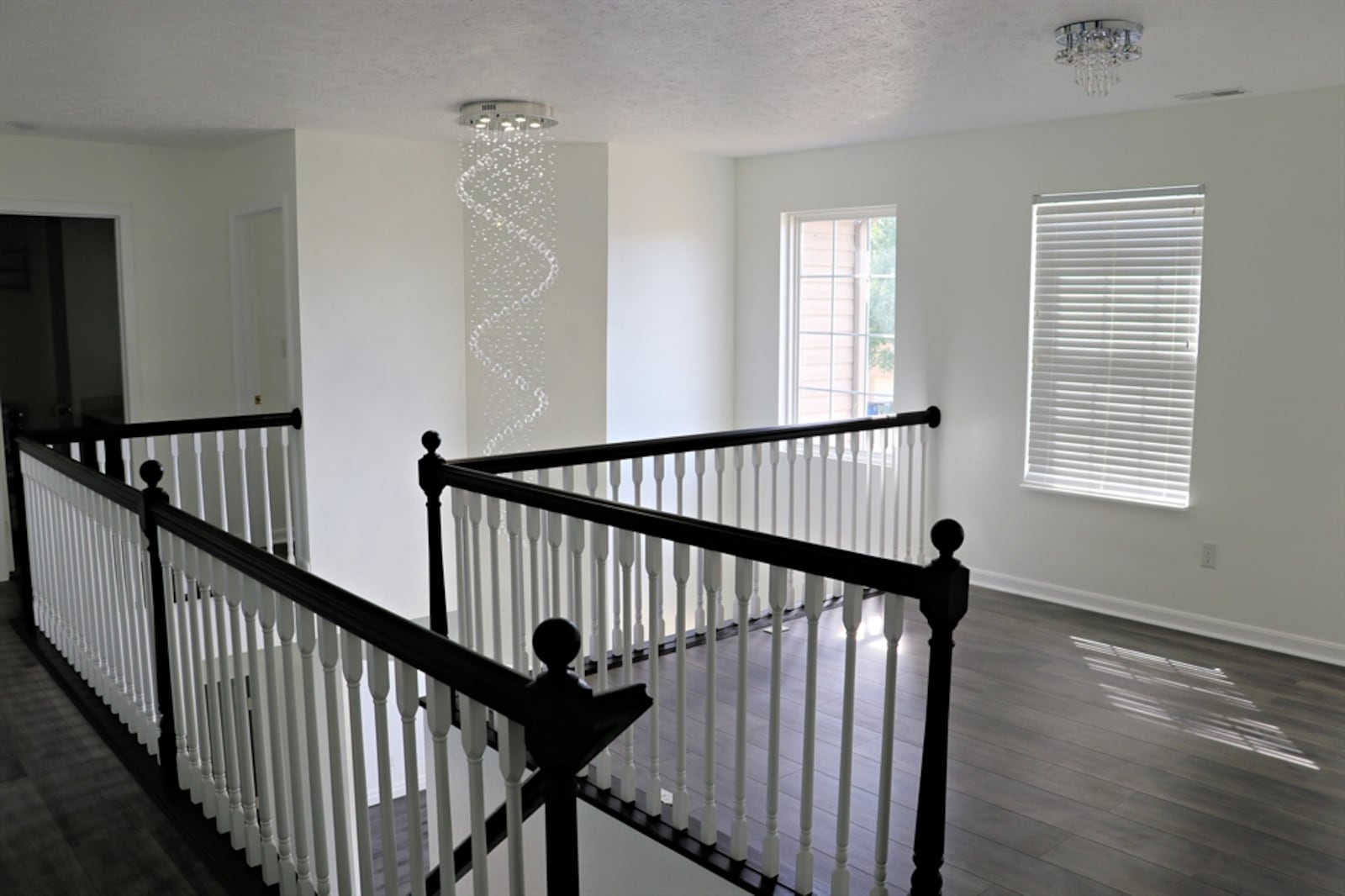 Contrasting white spindles with a dark railing wrap along the open wooden staircase to the second-floor loft family room and balcony hallway. 