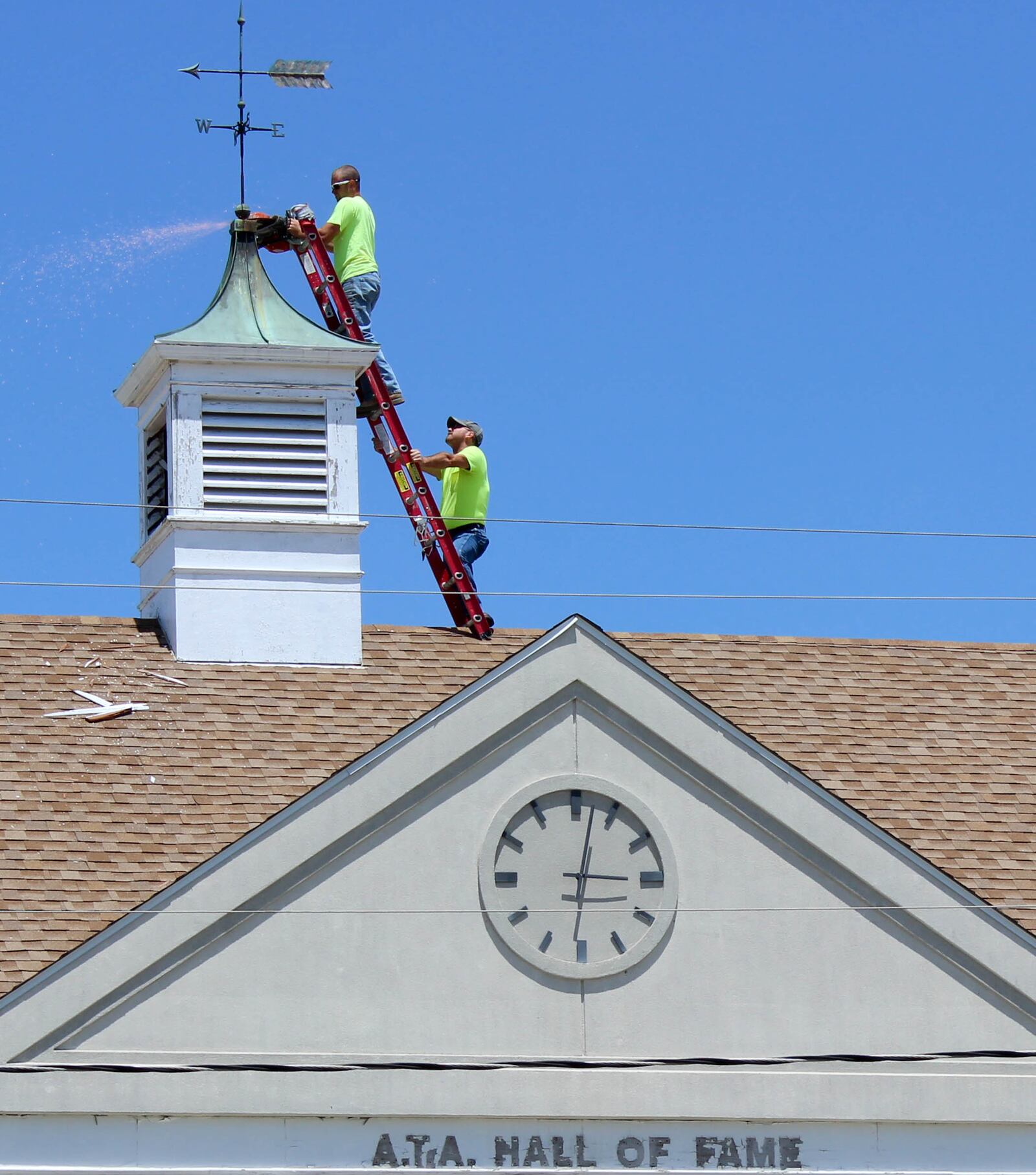 As a sign of an end of an era, City of Dayton contractors Adam Bradford, top and Dave Hall remove the weather vane on top of the vacant  Amateur Trapshooting Association Hall of Fame Building in Vandalia. The weather vane is going to be restored and likely moved to a historical society. CHUCK HAMLIN/ STAFF