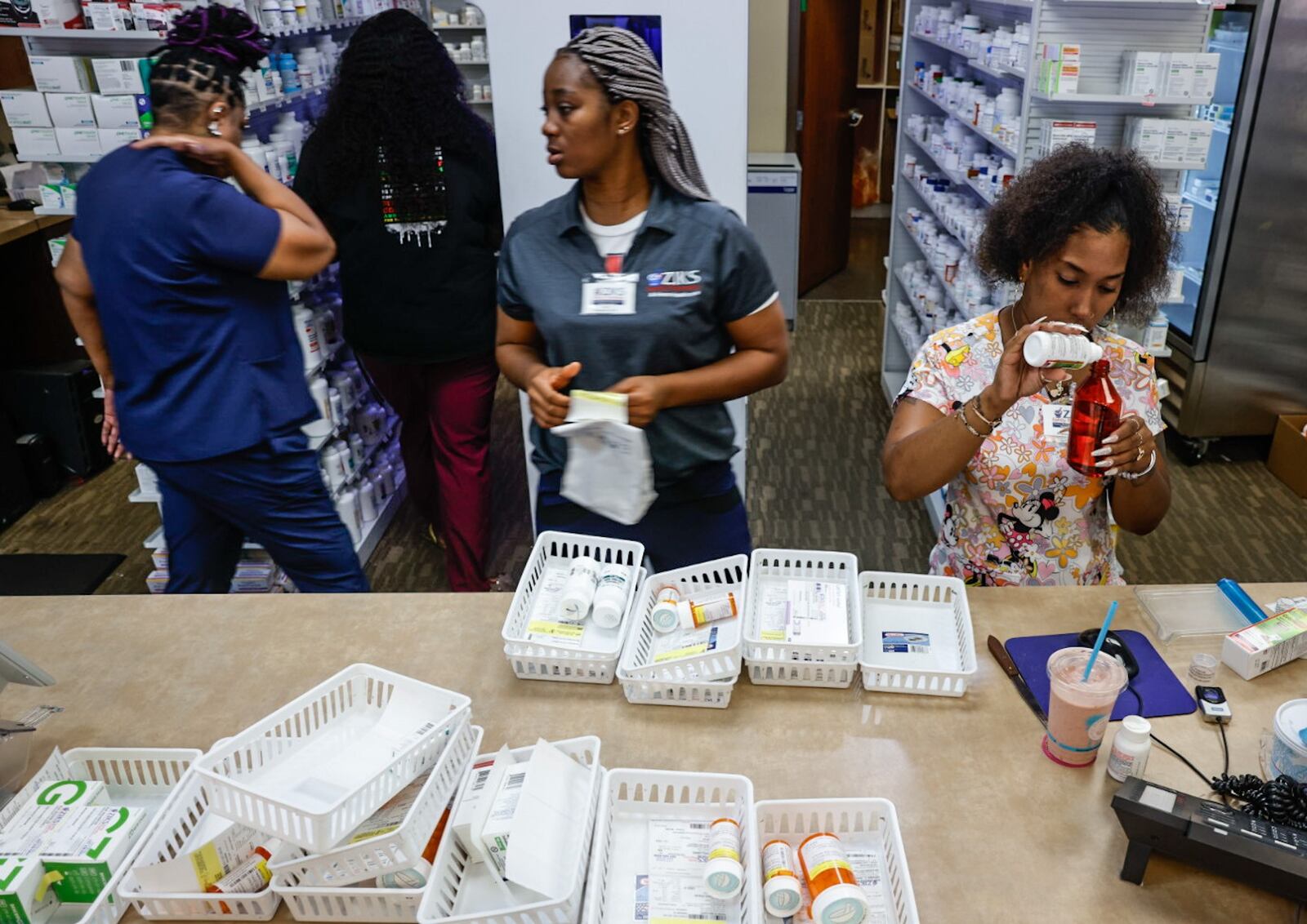 Pharmacy technicians for Ziks Pharmacy on West Third Street Jasmine Woodard, right and Joy Duaka, center, prep medications at the store on Monday, July 1, 2024. The closing of many pharmacies around Dayton is making it harder for residents to get their medications and harder for the pharmacies left to meet growing demands. JIM NOELKER/STAFF