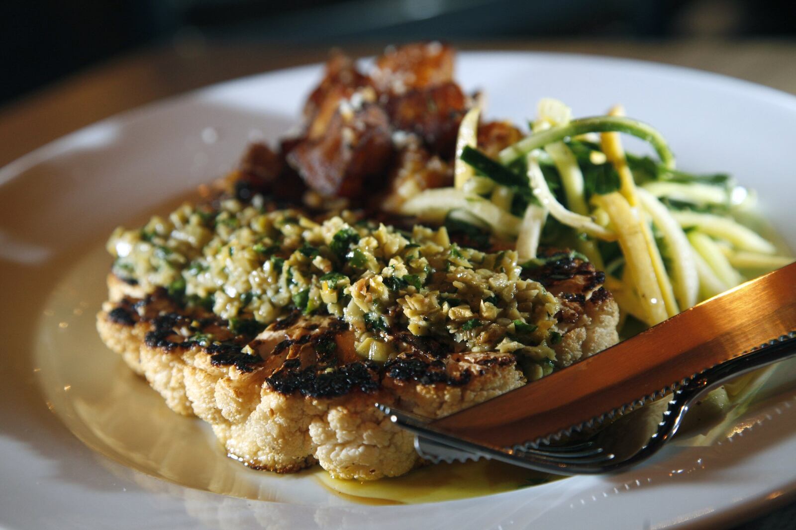 Wheat Penny Oven and Bar serves a cauliflower t-bone served with roasted potatoes and zucchini with mint. The t-bone is garnished with chopped sauce made of olive, garlic, capers, raisins, orange segments herbs and olive oil. LISA POWELL / STAFF