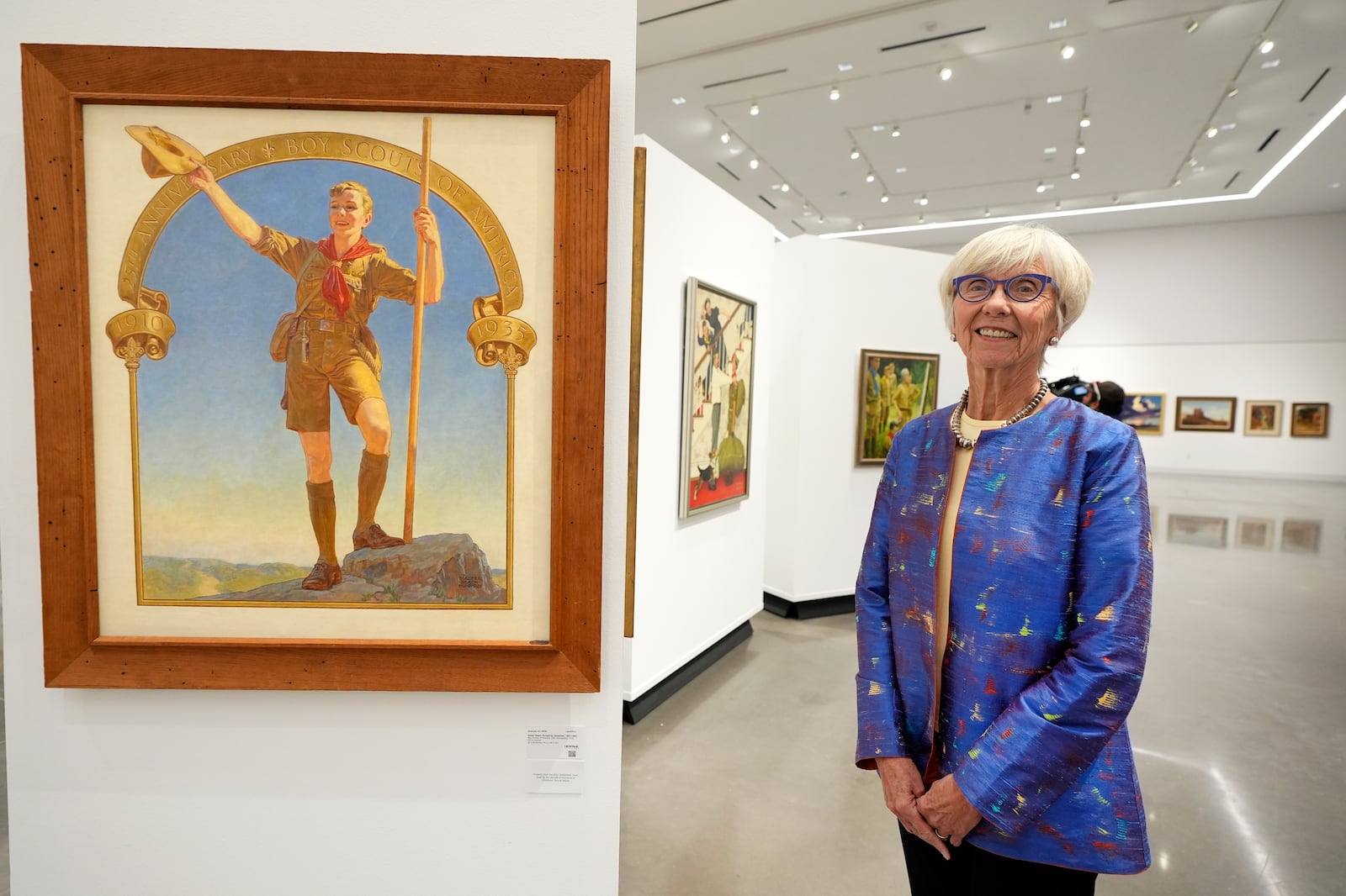 Judge Barbara Houser poses for a photo at Heritage Auctions in Dallas, Thursday, Oct. 17, 2024, by a collection of paintings from the Boy Scouts of America's storied collection that will be going up for auction. (AP Photo/Tony Gutierrez)