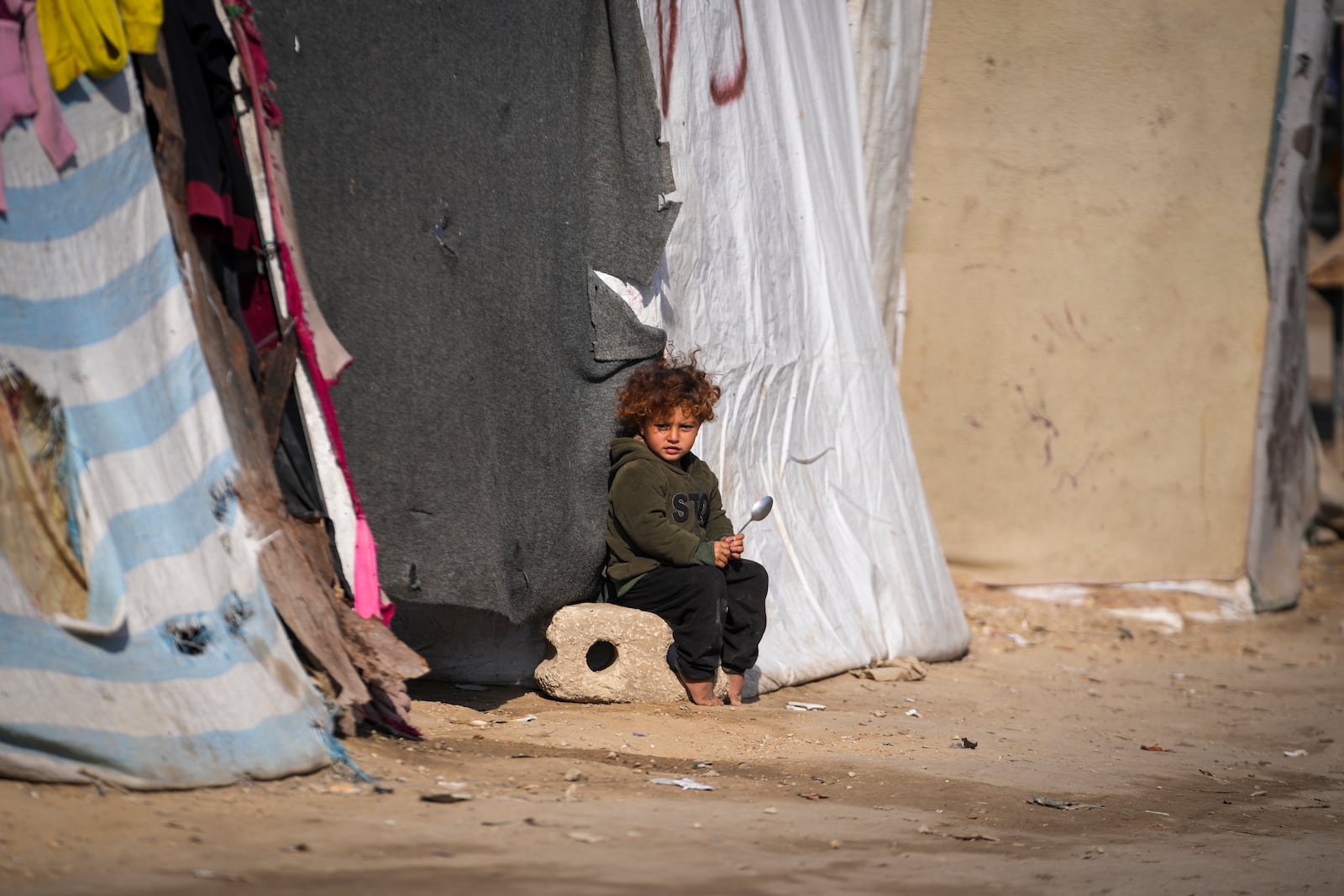 A child sits outside a tent at a camp for displaced Palestinians in Deir al-Balah, central Gaza Strip, Friday Jan. 17, 2025. (AP Photo/Abdel Kareem Hana)