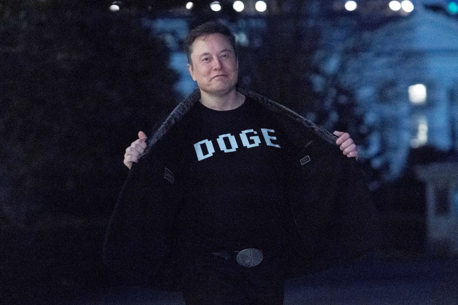 Elon Musk flashes his t-shirt that reads "DOGE" to the media as he walks on South Lawn of the White House, in Washington, Sunday, March 9, 2025. (AP Photo/Jose Luis Magana)