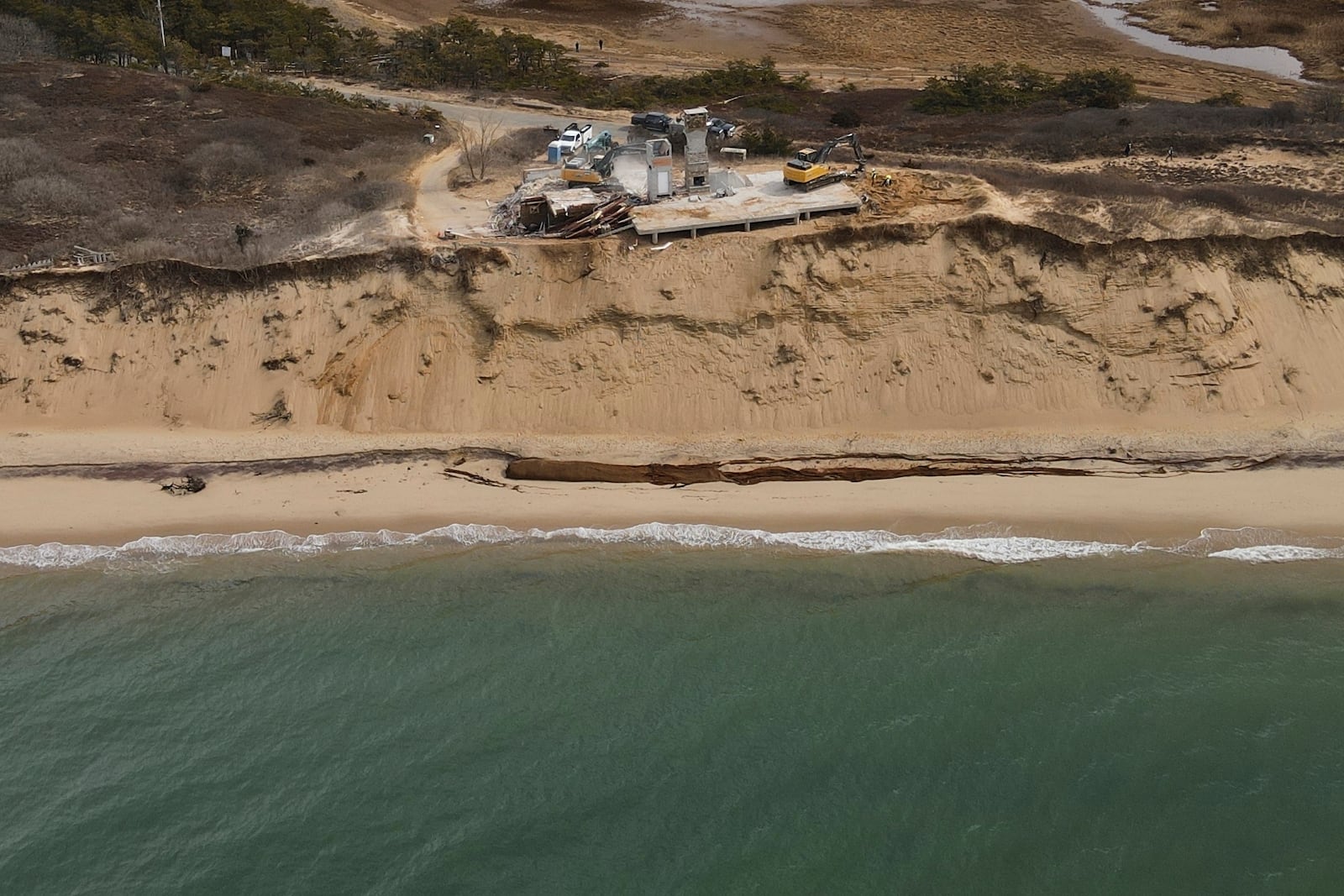 The remains of a home sit atop of a sandy bluff overlooking a beach in Wellfleet, Mass., Tuesday, Feb. 25, 2025. (AP Photo/Andre Muggiati)