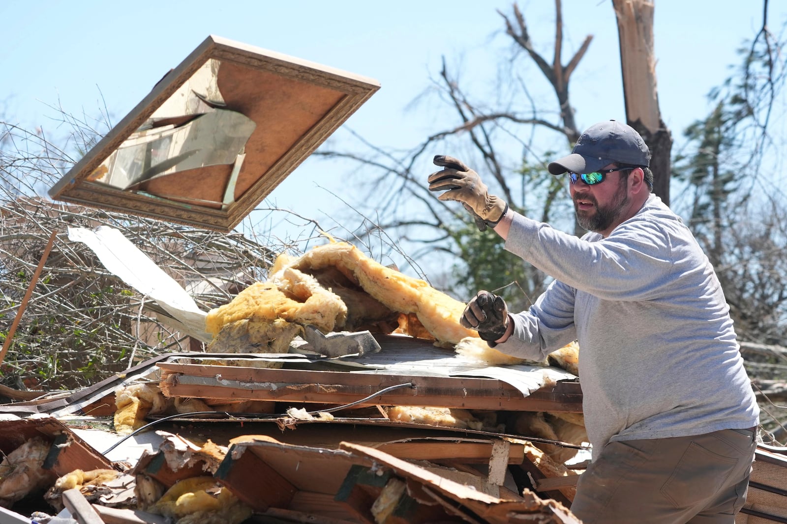 Tommy May, tosses a broken mirror from a tornado destroyed home of relatives, Sunday, March 16, 2025, in Tylertown, Miss. (AP Photo/Rogelio V. Solis)