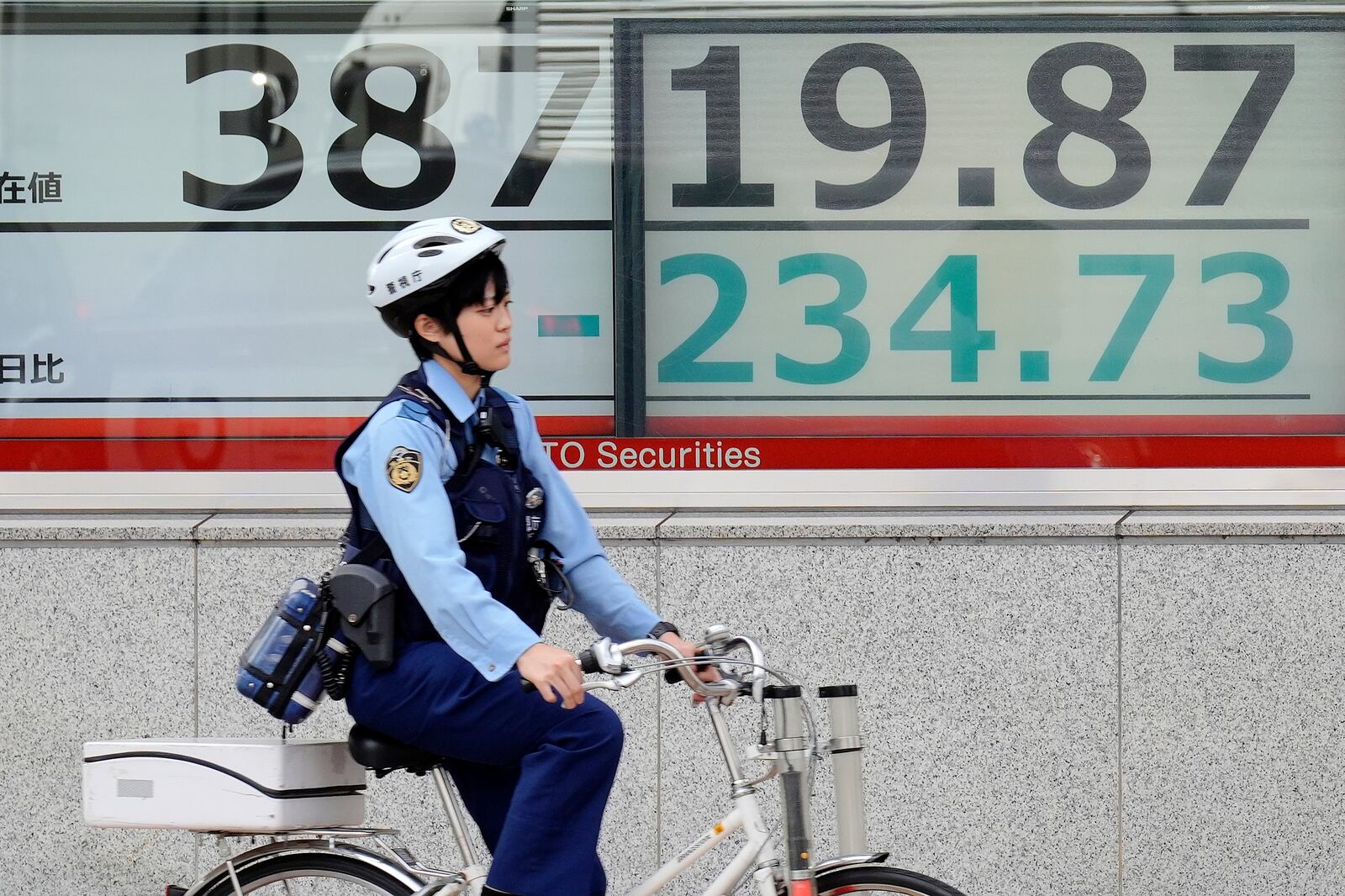 A police officer rides a bicycle in front of an electronic stock board showing Japan's Nikkei index at a securities firm Tuesday, Oct. 22, 2024, in Tokyo. (AP Photo/Eugene Hoshiko)