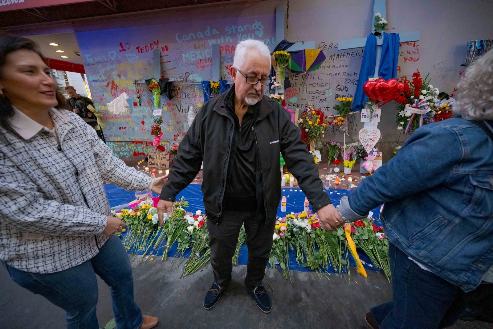 Long Island, New York residents Louis Tenedorio holds hands with family friend Angelique Whittington, left, and his wife, Cathy Tenedorio, by a memorial on Bourbon Street and Canal Street in New Orleans, Saturday, Jan. 4, 2025, where his son, Matthew Tenedorio, was killed as one of the victims of the New Year's Day deadly truck attack and shooting. (AP Photo/Matthew Hinton)