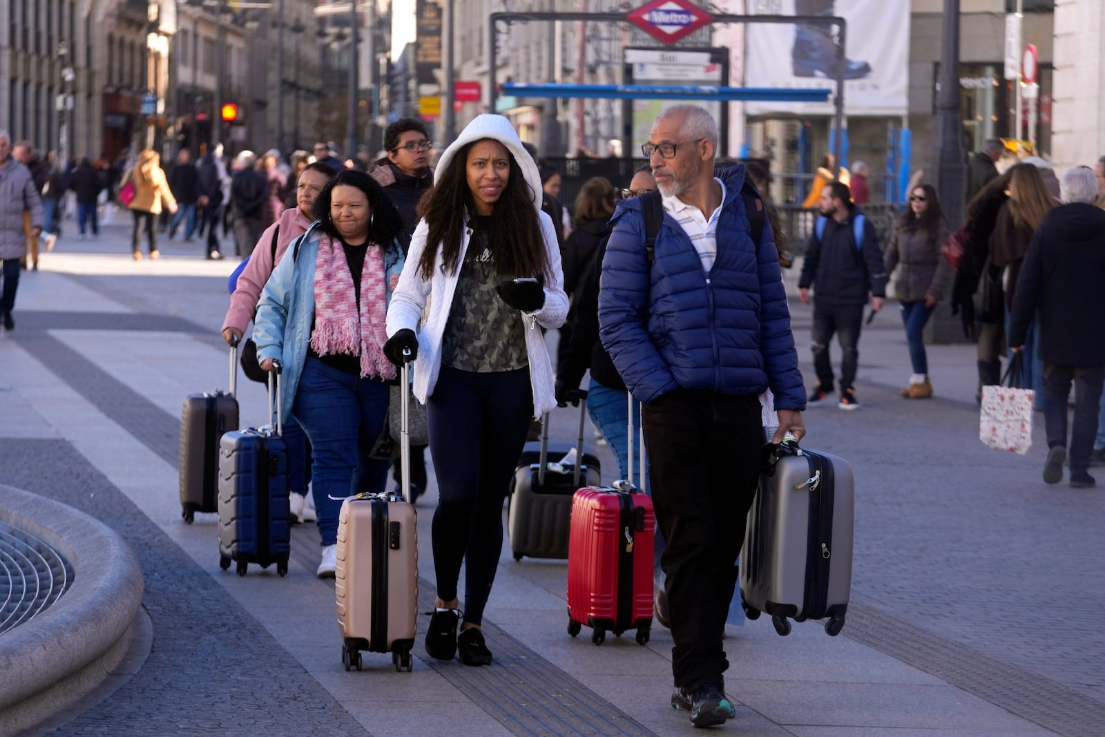 Tourists walk with suitcases in an area with short-term rentals on platforms, like AirBnB in Madrid, Spain, Tuesday, Jan. 14, 2025. (AP Photo/Paul White)