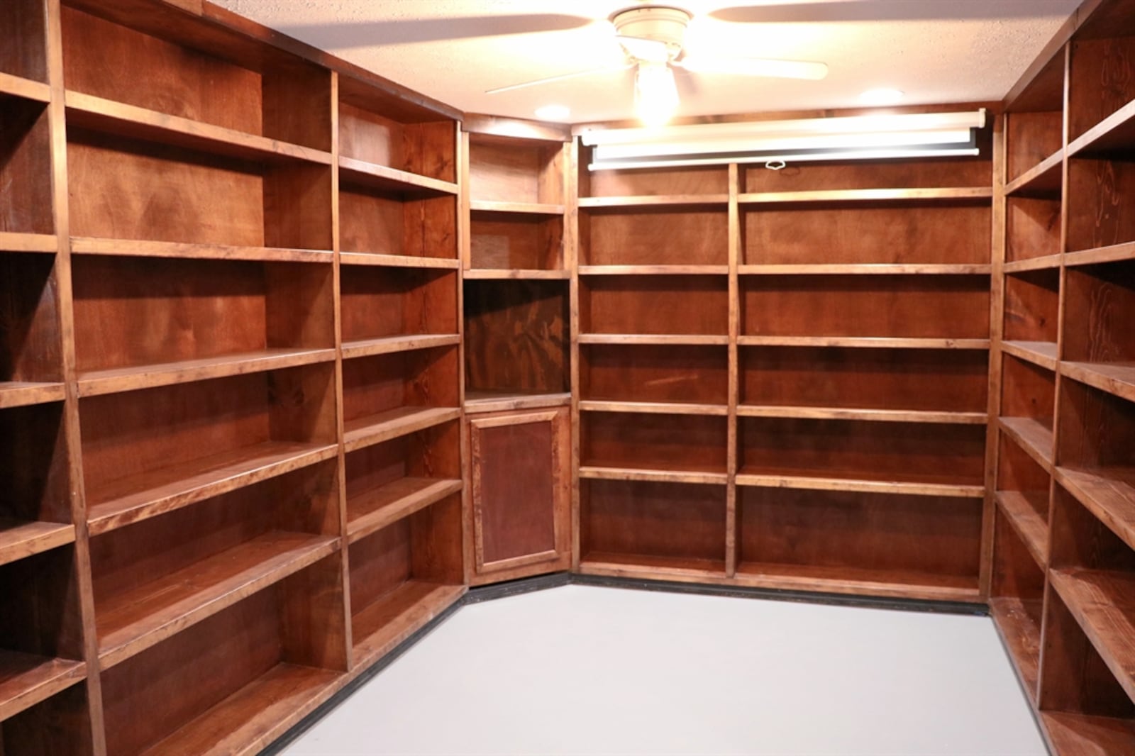 A library features four walls of built-in bookcases. The room is big enough for an office or sitting area. 