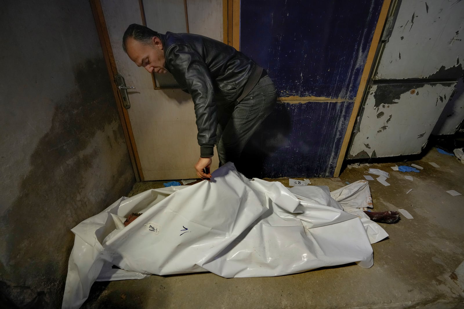 EDS NOTE: GRAPHIC CONTENT - A man examines a body wrapped in a plastic bag at the Al-Mojtahed Hospital in Damascus, Syria, on Wednesday, Dec. 11, 2024. Many are flocking to morgues, hoping to identify loved ones who have been killed or were imprisoned under the rule of President Bashar Assad, whose government collapsed over the weekend. (AP Photo/Hussein Malla)