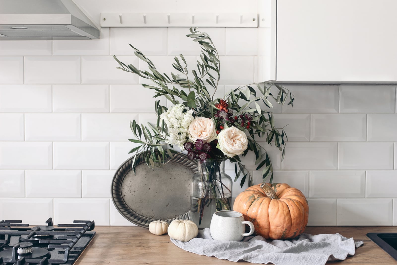 This autumn still life composition in a rustic eclectic kitchen interior includes a cup of coffee, vintage silver tray and floral bouquet. Bring artisanal pieces into your fall décor by using textured artisanal trays, created with terracotta, plaster, or copper, vintage brass candlesticks or handmade pieces. iSTOCK/COX