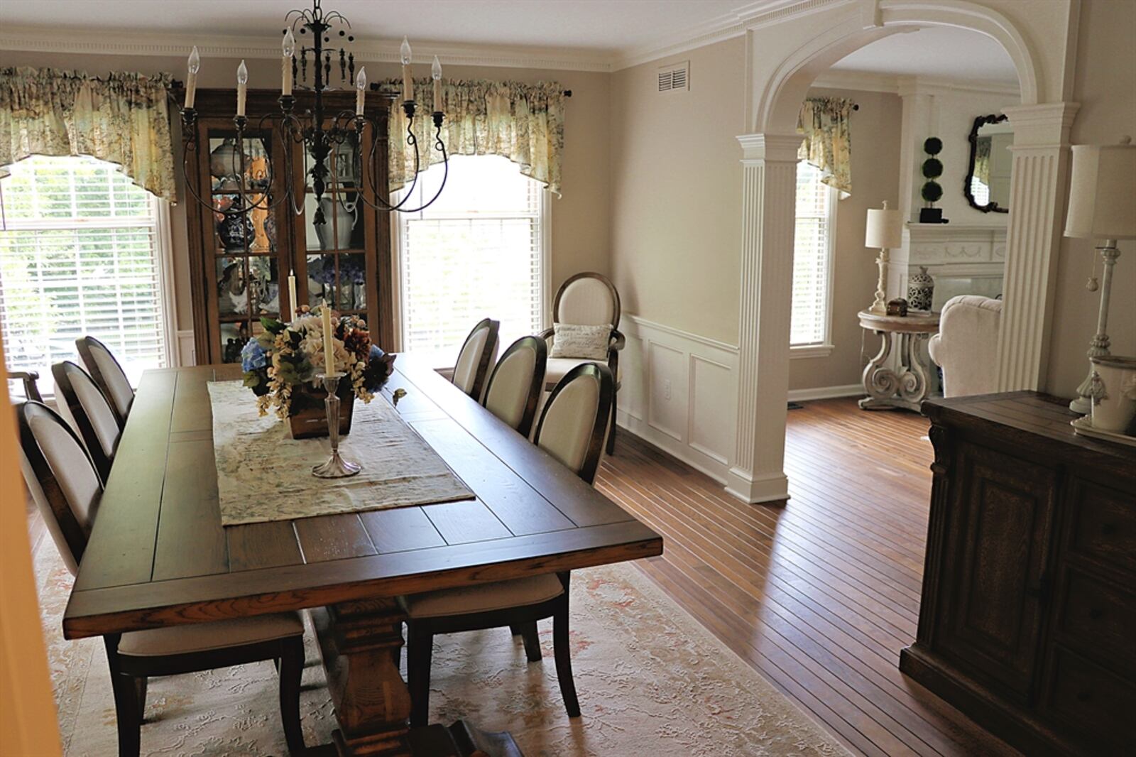 Hardwood flooring fills the living room and continues into the adjoining dining room, which has wainscoting and a grand chandelier.