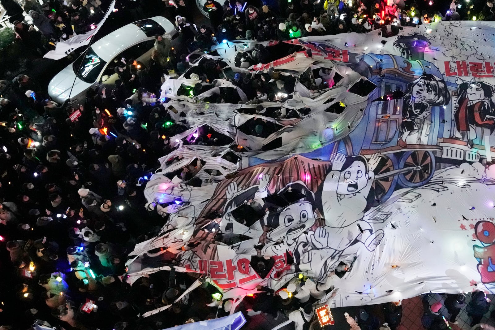 Participants tear a banner depicting South Korean President Yoon Suk Yeol's face on a cartoon train during a rally to demand his impeachment in front of the headquarters of the ruling People Power Party in Seoul, South Korea, Friday, Dec. 13, 2024. (AP Photo/Ahn Young-joon)