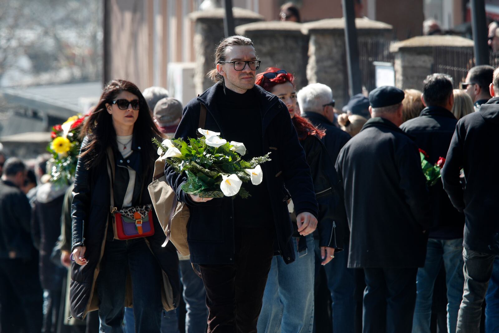 People carrying flowers arrive for the funeral of Andrej Gjorgieski, one of the lead singers of Macedonian band DNK, a victim of the March 16 nightclub fire in the town of Kocani, at a cemetery in Skopje, North Macedonia, Thursday, March 20, 2025. (AP Photo/Boris Grdanoski)