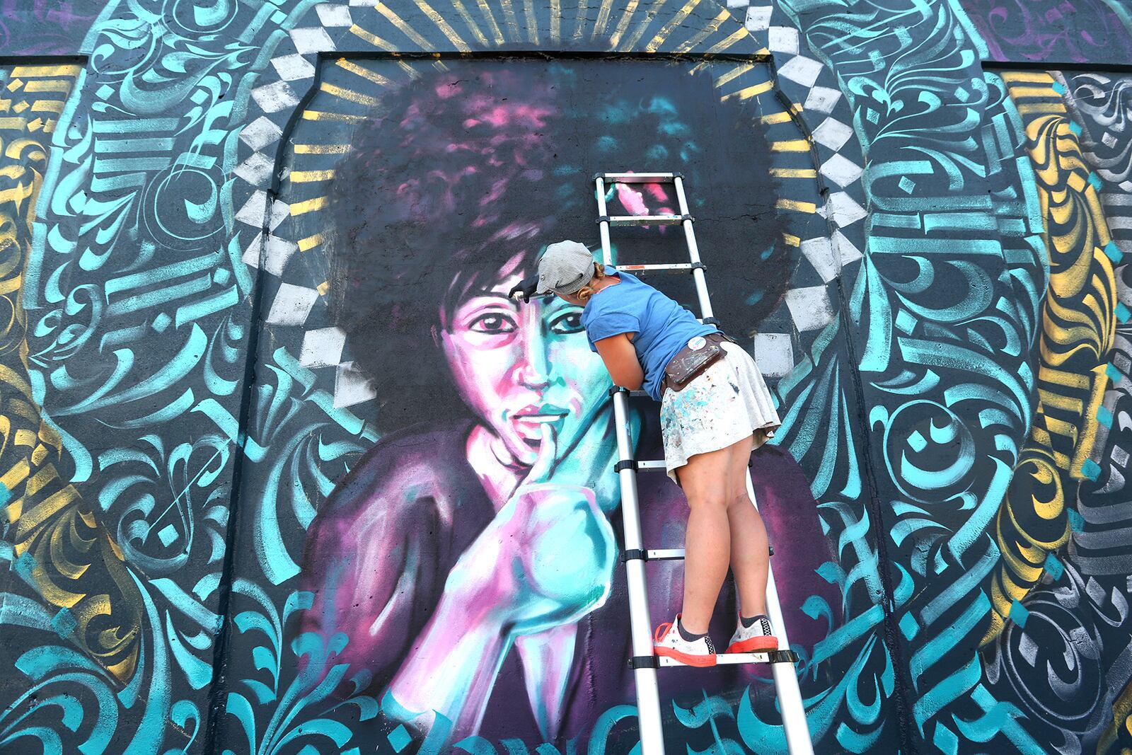 Tiffany Clark, founder of the Mural Machine, is creating a new mural at the entrance of the Oregon District in Dayton. The mural, created with brush and spray paint in 20 colors, depicts a woman at the center.  LISA POWELL / STAFF