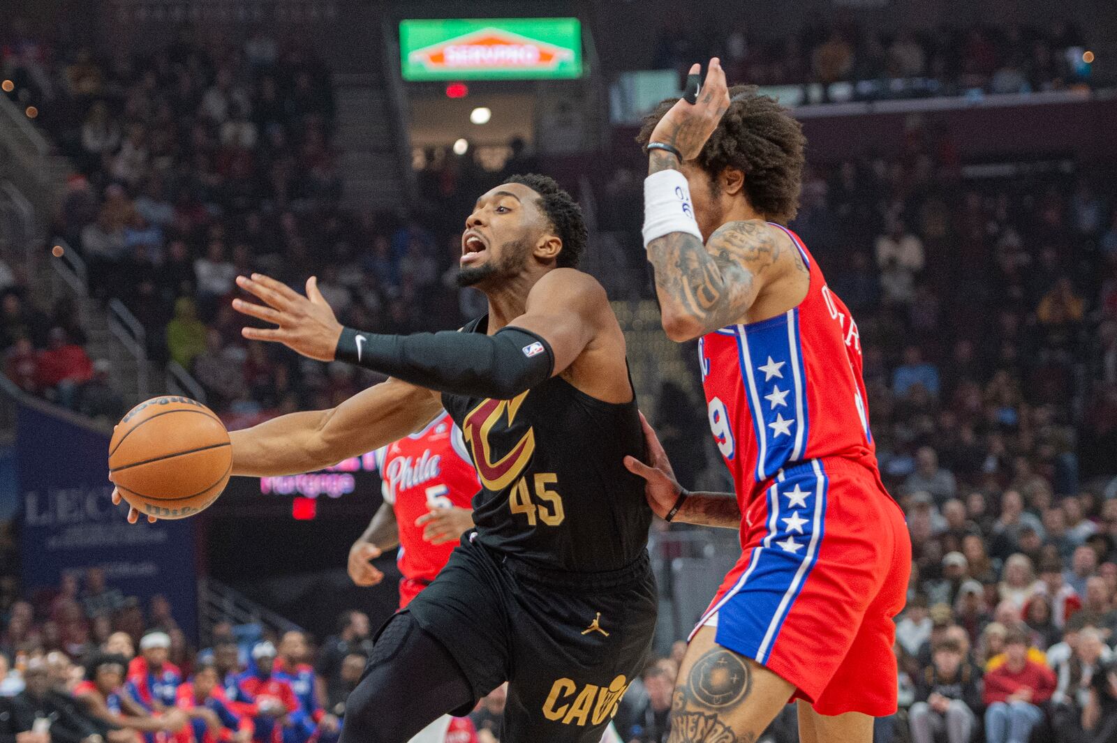 Cleveland Cavaliers' Donovan Mitchell (45) drives to the basket as Philadelphia 76ers' Kelly Oubre Jr., right, defends during the first half of an NBA basketball game in Cleveland, Saturday Dec. 21, 2024. (AP Photo/Phil Long)