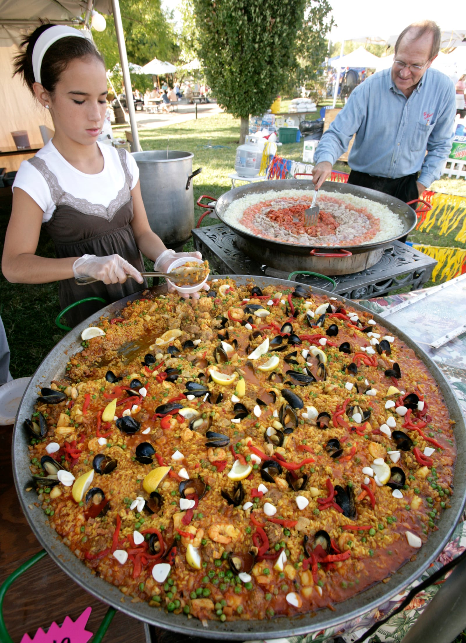 9-278-07--Photo by Ty Greenlees--Anna Castro, left, served Paella as El Meson chef Mark Abbott started another paellera pan full of the seafood and garlic dish at the 2007 Garlic Festival at Cox Arboretum Metro Park on Friday evening.  The festival continues on Saturday 11-7 and Sunday 11-5.