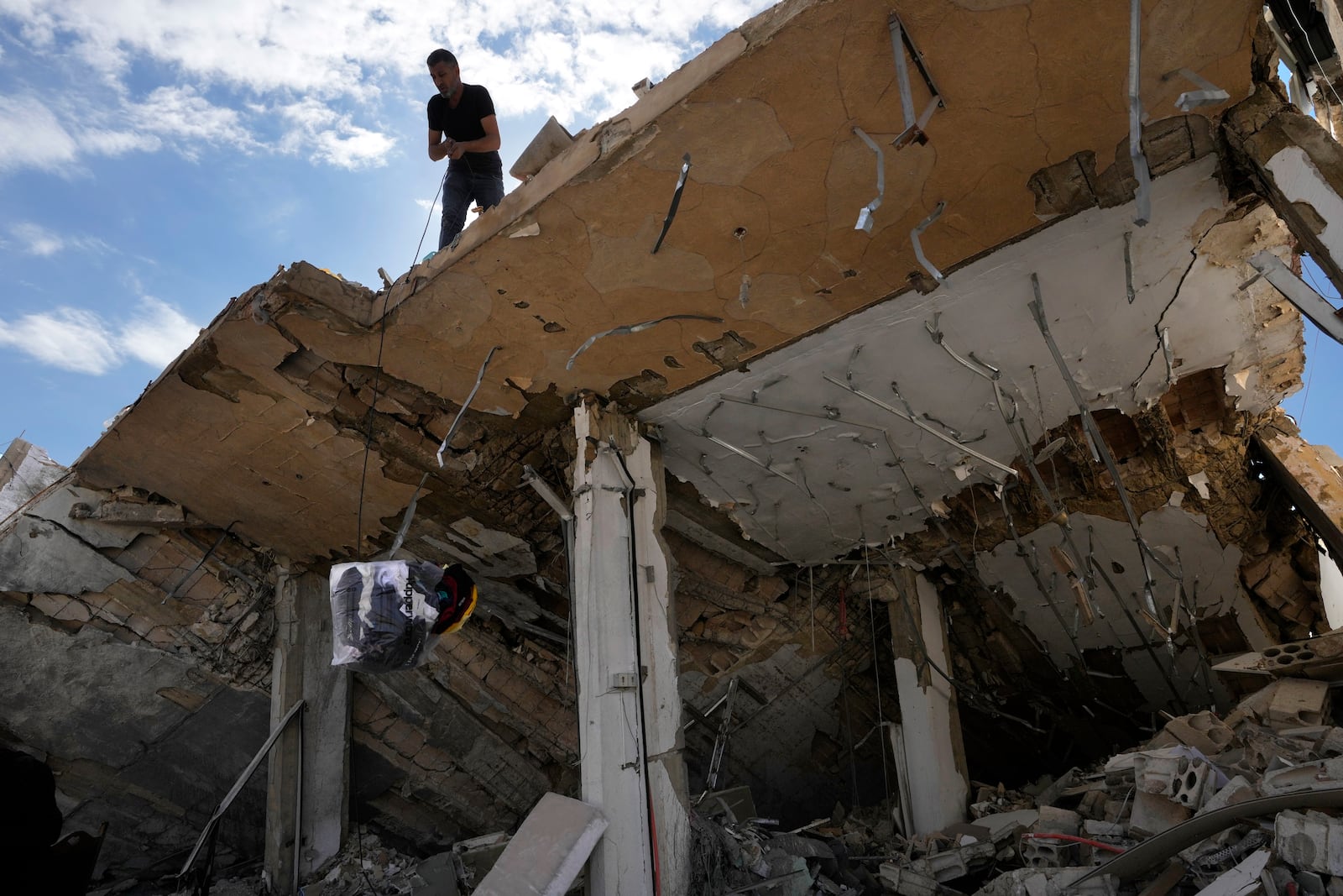 A man lowers a bag of his family's clothing from the roof of his destroyed house after he returned to his village of Hanouiyeh, southern Lebanon, Thursday, Nov. 28, 2024 following a ceasefire between Israel and Hezbollah that went into effect on Wednesday. (AP Photo/Hussein Malla)