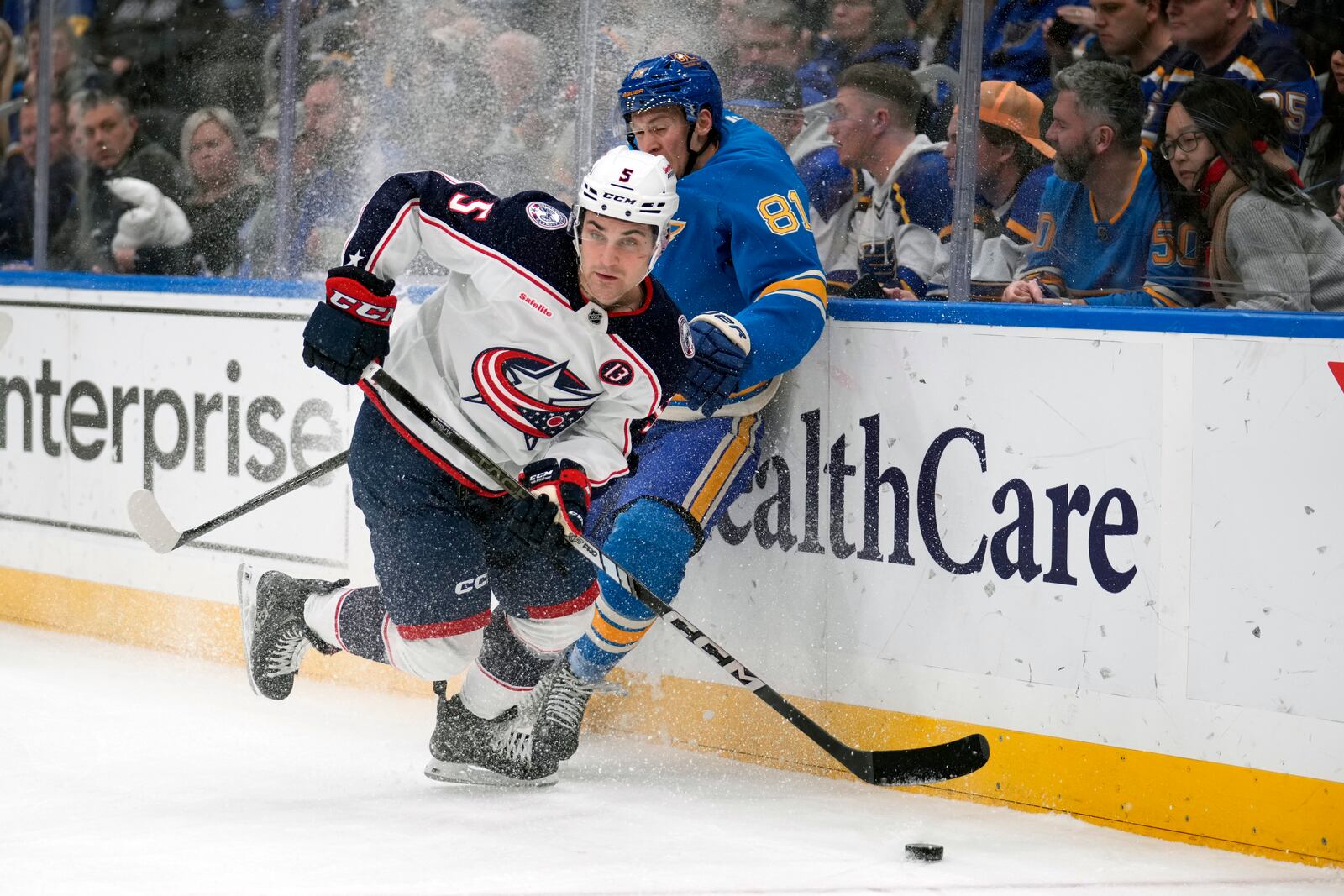 Columbus Blue Jackets' Denton Mateychuk (5) looks to pass as St. Louis Blues' Dylan Holloway (81) slams into the boards during the second period of an NHL hockey game Saturday, Jan. 11, 2025, in St. Louis. (AP Photo/Jeff Roberson)