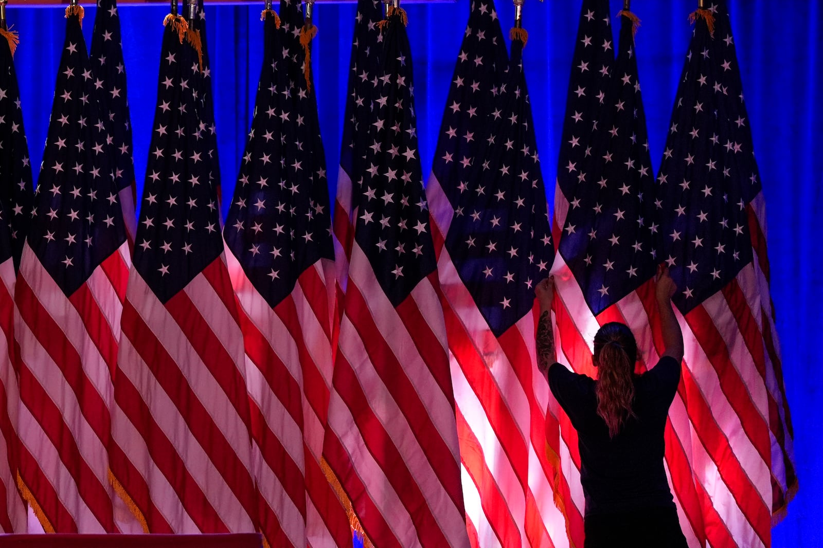 A worker adjusts the flags on stage ahead of an election night watch party for Republican presidential nominee former President Donald Trump Tuesday, Nov. 5, 2024, in West Palm Beach, Fla. (AP Photo/Julia Demaree Nikhinson)