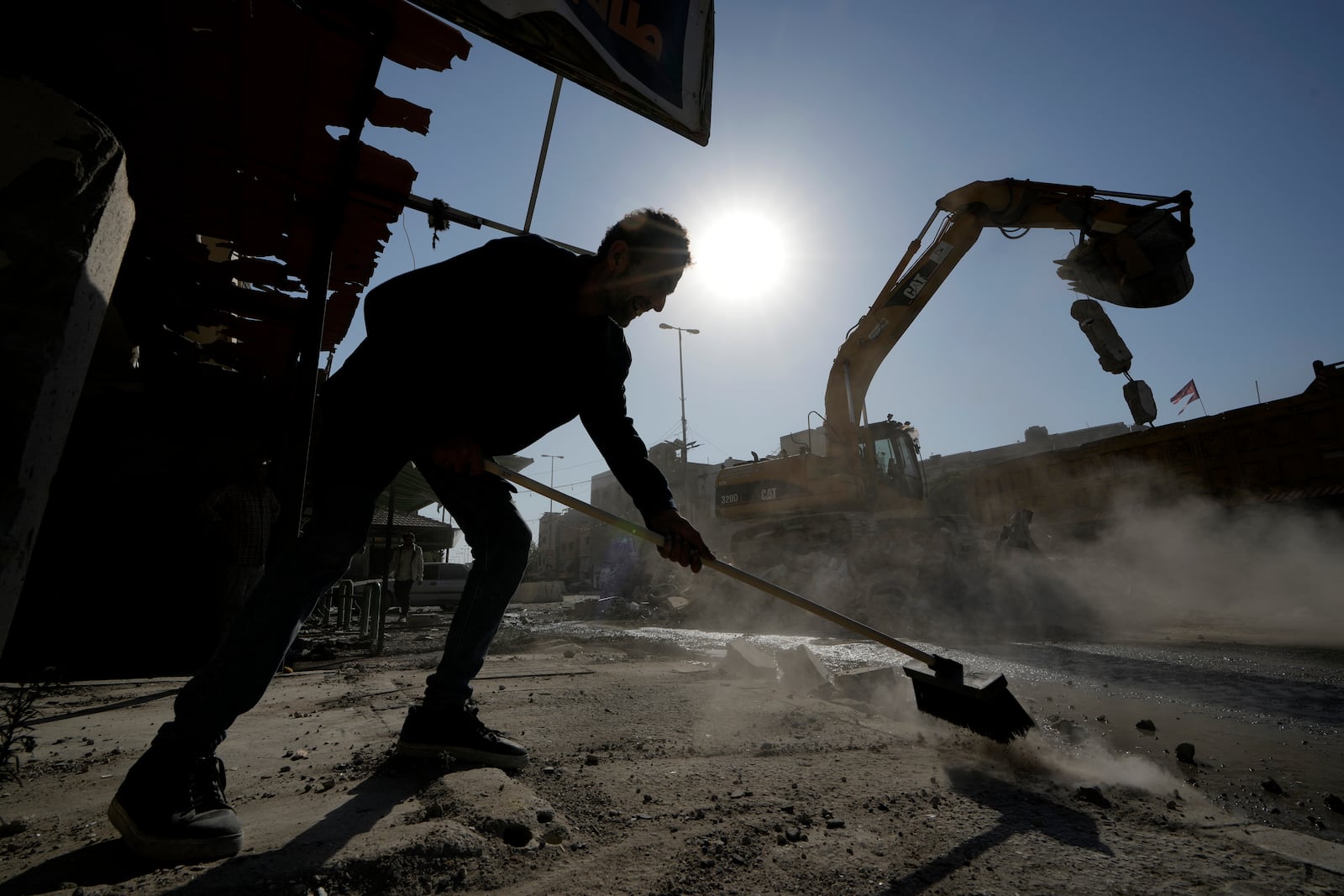 A man removes the debris from a street in front of a destroyed building that was hit Tuesday night in an Israeli airstrike, in the southern port city of Sidon, Lebanon, Wednesday, Oct. 30, 2024. (AP Photo/Bilal Hussein)