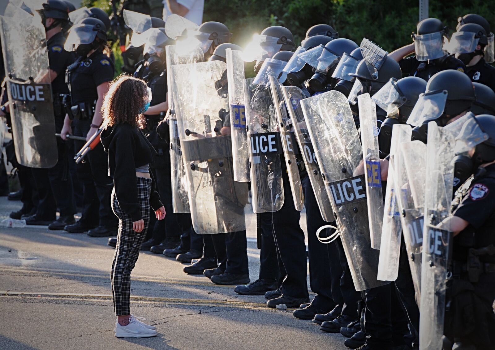 A girl stands in front of Dayton police officers in riot gear during protests Saturday, May 30, 2020, in Dayton. MARSHALL GORBY / STAFF