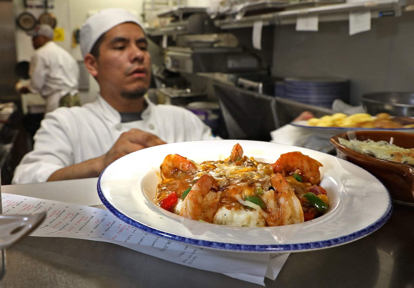 Chef Julio Mira serves up some shrimp and grits in the kitchen at Ellie’s Restaurant & Bakery in the Mills Park Hotel in Yellow Springs. BILL LACKEY/STAFF