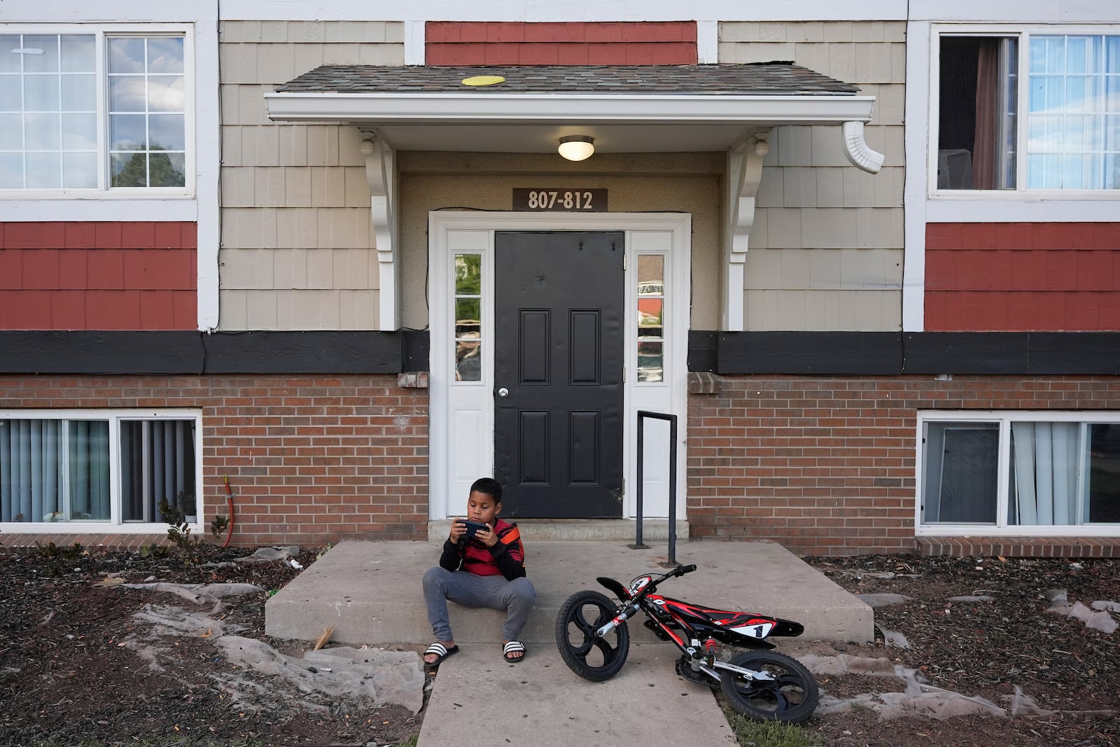 Dylan Martínez-Ramírez plays a game on his mother's cell phone outside their apartment Thursday, Aug. 29, 2024, in Aurora, Colo. (AP Photo/Godofredo A. Vásquez)