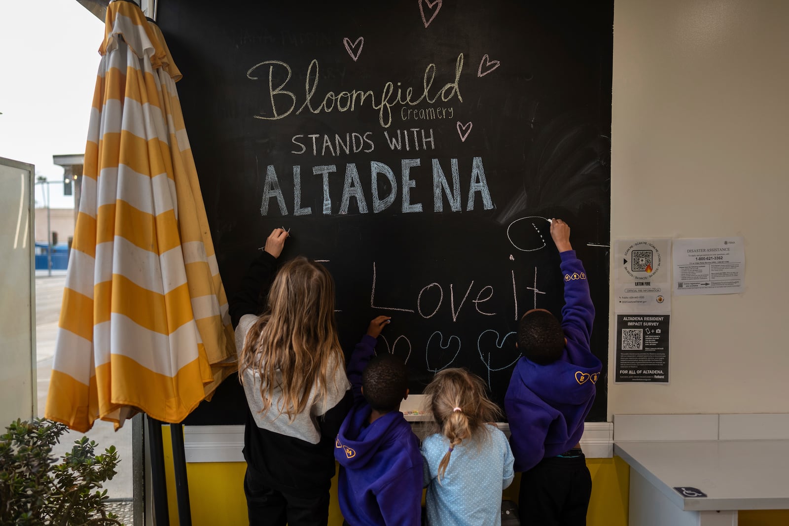 Eaton Fire evacuees Ceiba Phillips, from left, Russell Graham, Ceiba's sister, Quoia, and Russell's brother, Justin, draw on a blackboard at an ice cream shop in Pasadena, Calif., Wednesday, Feb. 5, 2025. (AP Photo/Jae C. Hong)