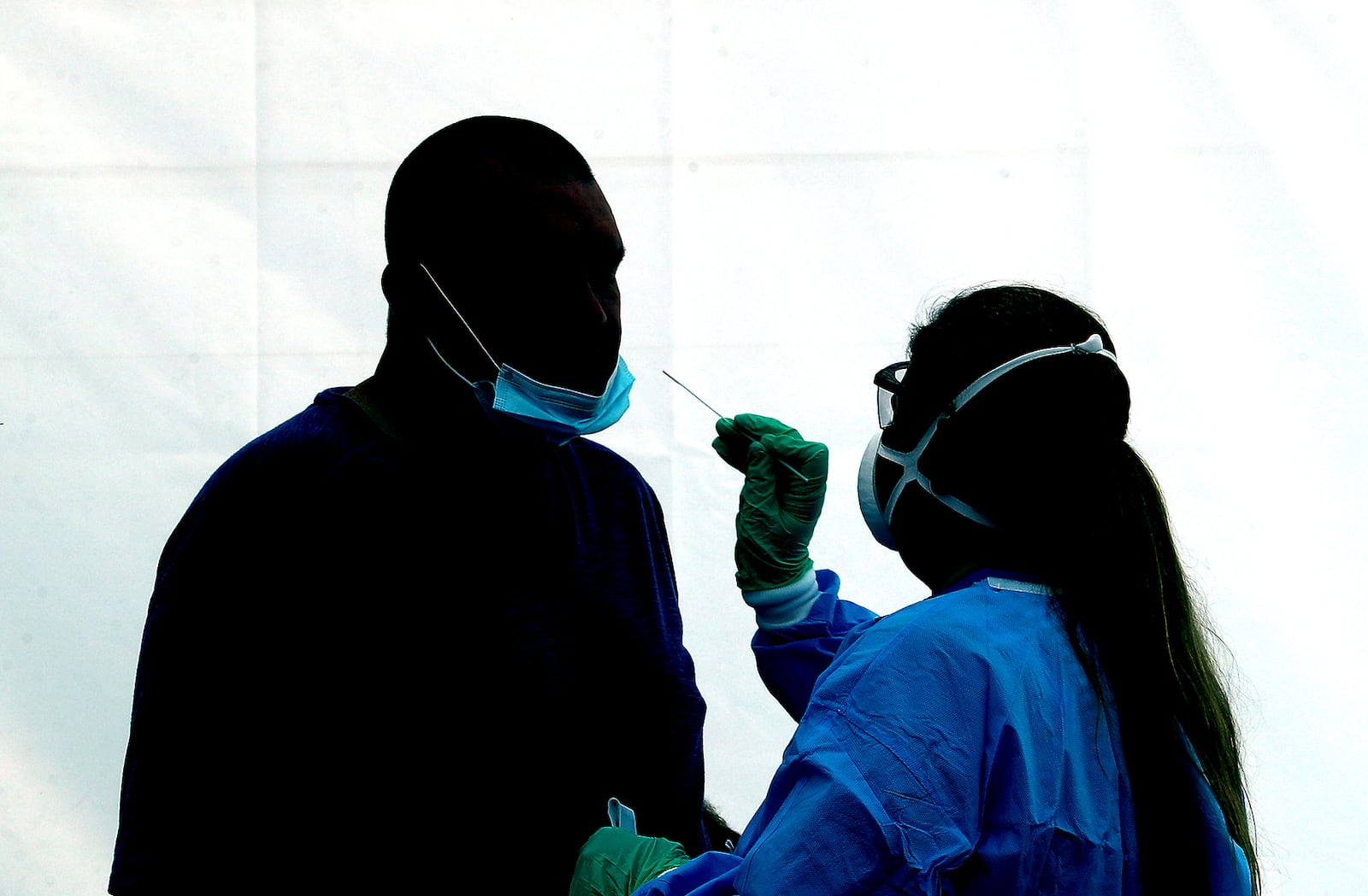 A man is silhoutted against the wall of a white tent as he gets a COVID-19 test Wednesday at the Clark County Combined Health District's free COVID testing clinic at Hayward Middle School. BILL LACKEY/STAFF