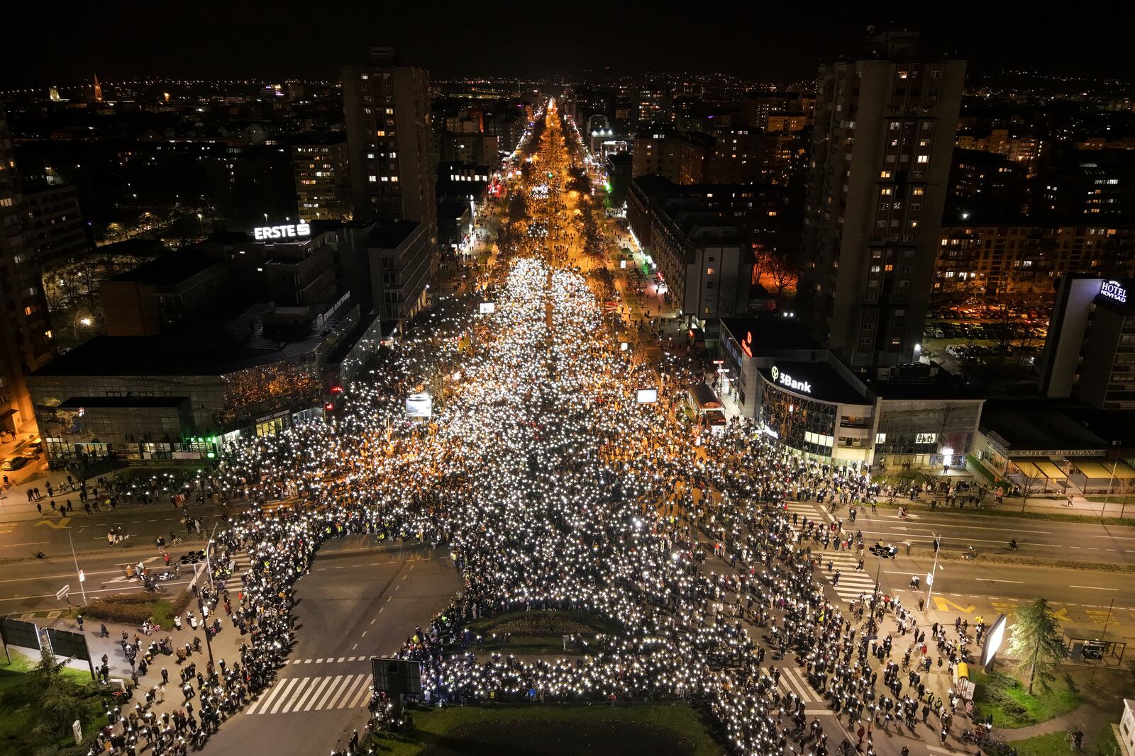 An aerial view of people hold up their mobile phone lights during a protest in front of a railway station where the collapse of a concrete canopy killed 15 people more than two months ago, in Novi Sad, Serbia, Friday, Jan. 31, 2025. (AP Photo/Armin Durgut)