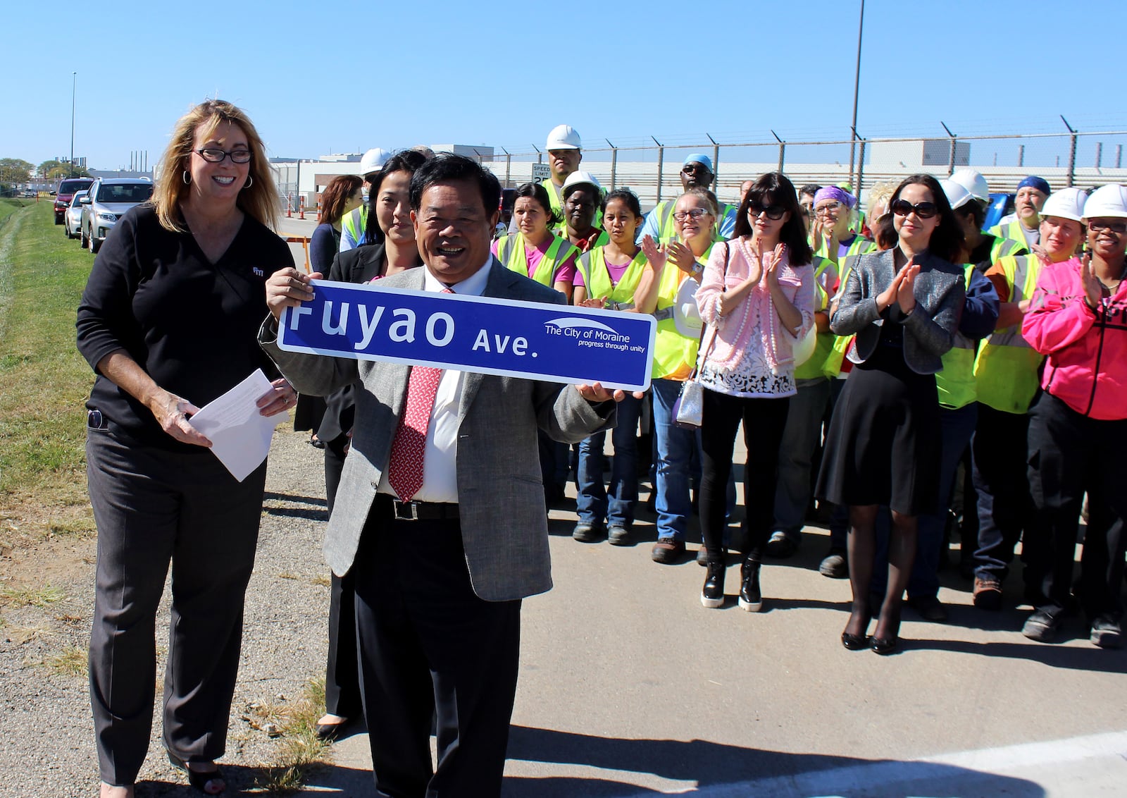 Moraine Mayor Elaine Allison and Fuyao Chairman Cao Dewang display the Fuayo Avenue street sign during dedication cerimonies in front of factory workers.